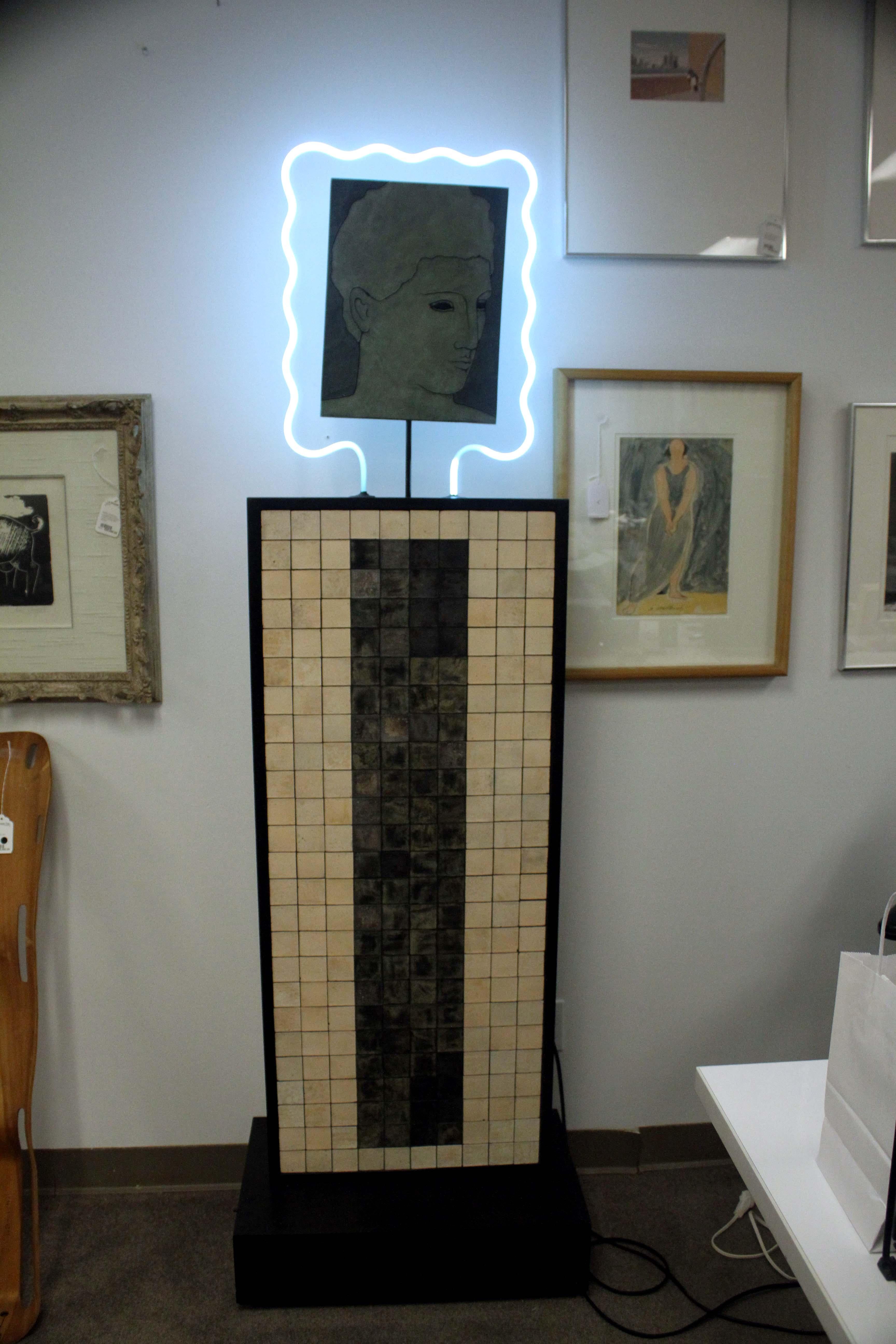An artful post modern sculpture depicting a Roman-Greco portrait on a ceramic tiled pedestal base. Signed Snyderman 1988. Attributed to American artist and gallerist Evan Snyderman. A curvy neon light outlines the portrait making a unique statement.