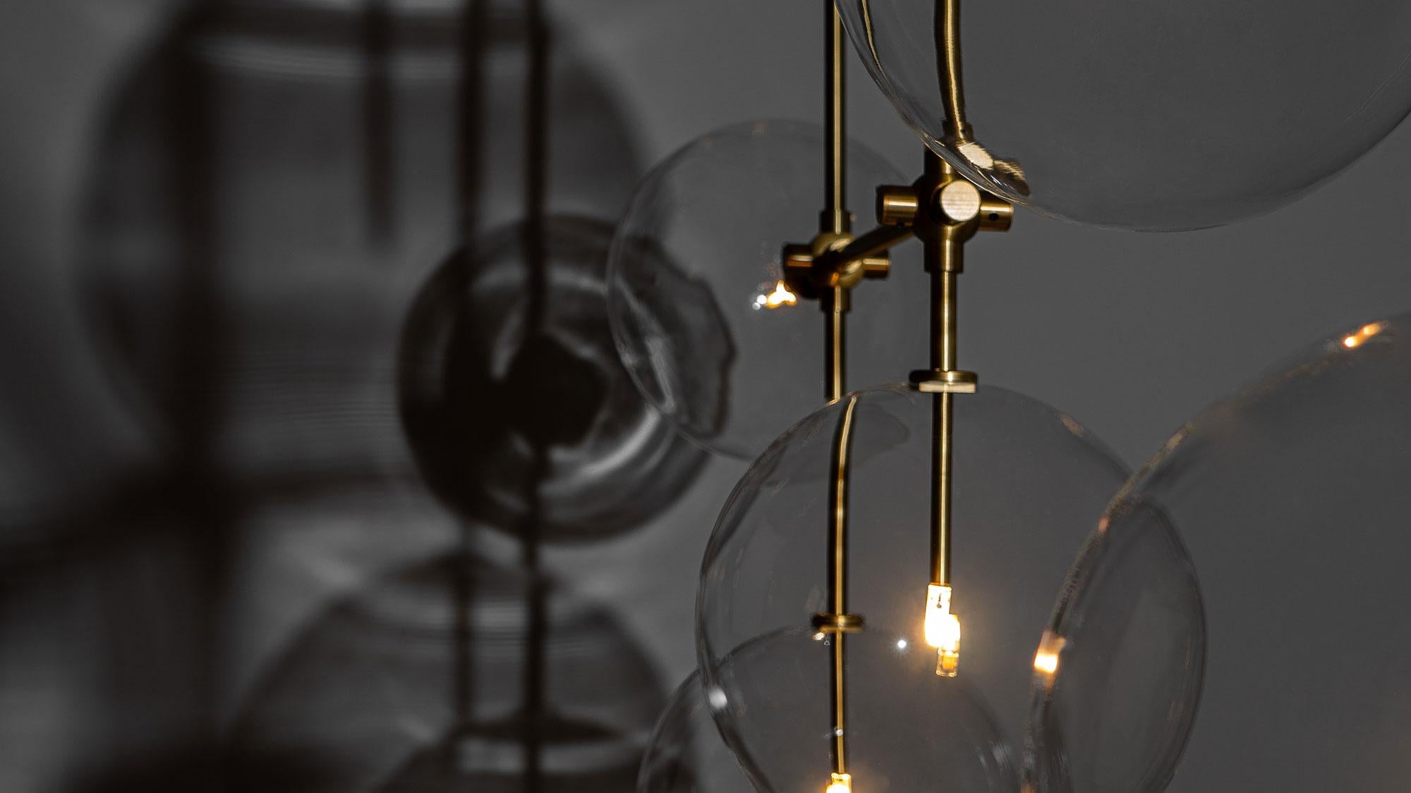 An array of ethereal glass globes floats weightlessly around a right-angled geometric lattice. The mouth-blown spheres are positioned rotationally around the brass grid, a spatial design creating an architectural impression.

Available in our