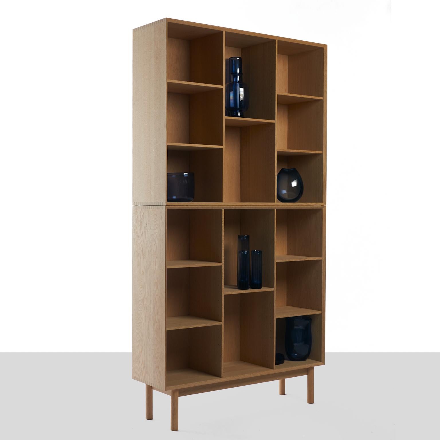 A tall bookcase shown in oak with a soaped finish. Exposed finger joints and adjustable shelves. Comprised of two stackable tops on a base with 4 feet. Designed by Peter Hvidt produced by Søborg Møbler in the original factory.