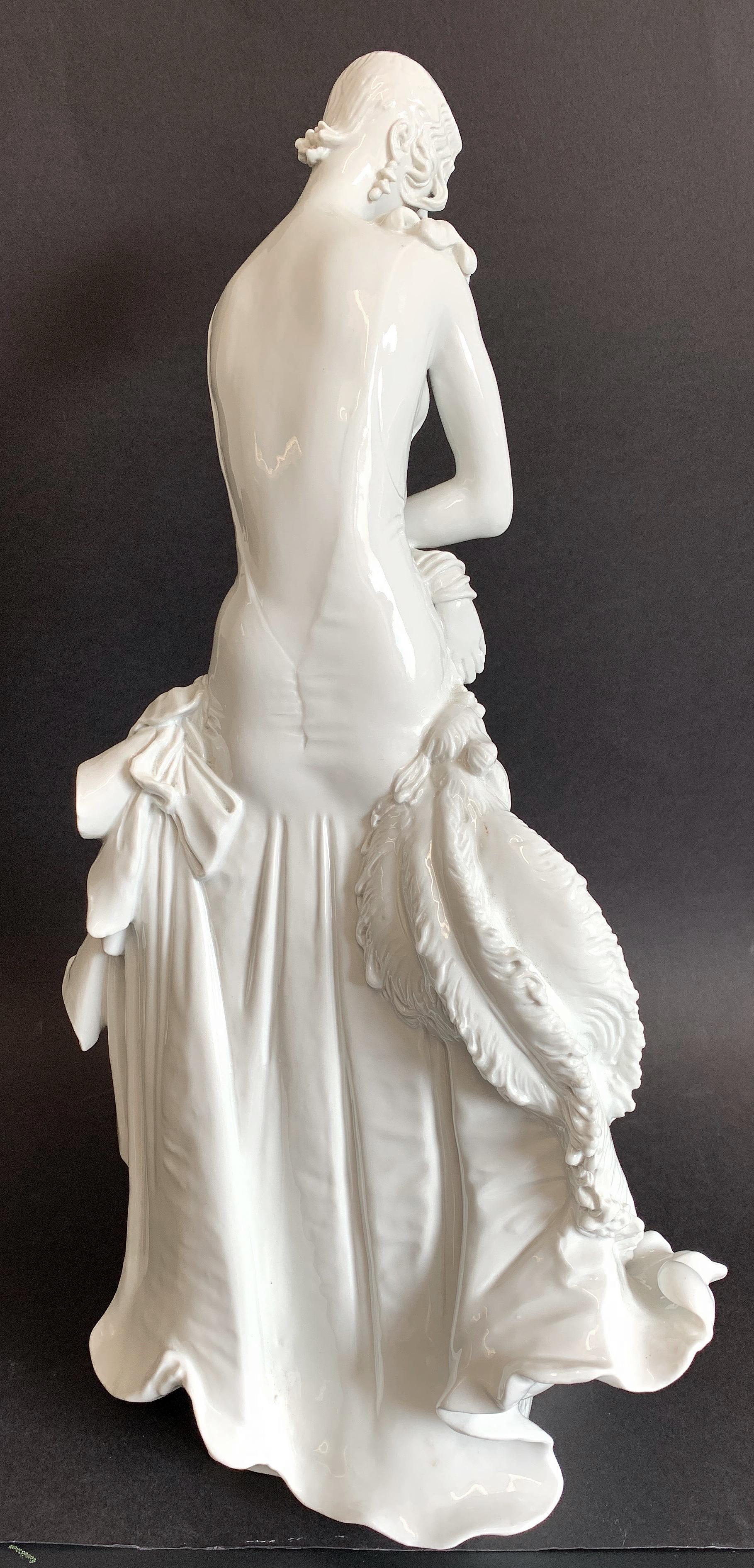 One of the most sophisticated and detailed depictions of Art Deco elegance and fashion we have ever offered, this 1929-era porcelain sculpture depicts a tall, beautiful woman, gorgeously attired, holding an ostrich fan and looking downward. The