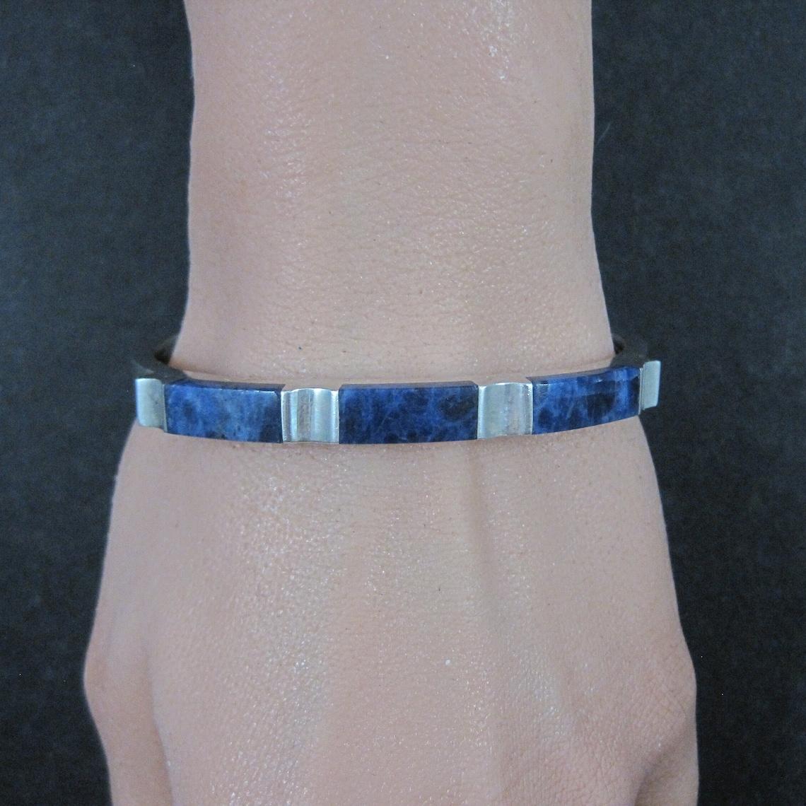 Ce magnifique bracelet mexicain vintage est en argent sterling et contient des pierres précieuses en sodalite.

Ce bracelet mesure un quart de pouce de large et s'amincit de 3 à 6 mm d'épaisseur.
Il a une circonférence intérieure de 6 1/2 pouces et