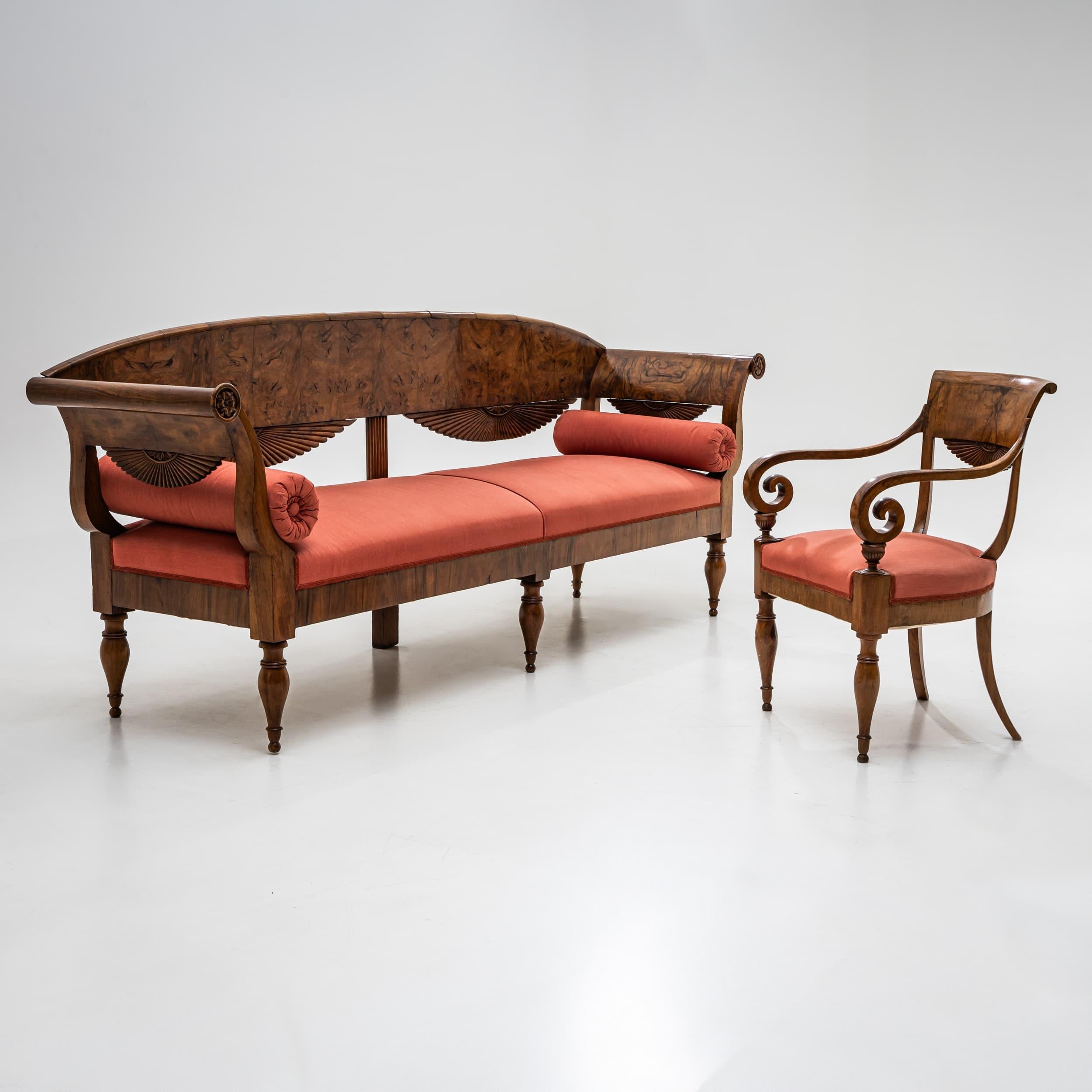 Eine elegante Sitzgruppe bestehend aus einem Sofa mit geschwungener Rückenlehne und einem passenden Sessel (86 x 56 x 55 x 50 cm). Beide Stücke sind aus Nussbaumholz gefertigt und verfügen über anmutig geschnitzte Voluten und ein Ornament im