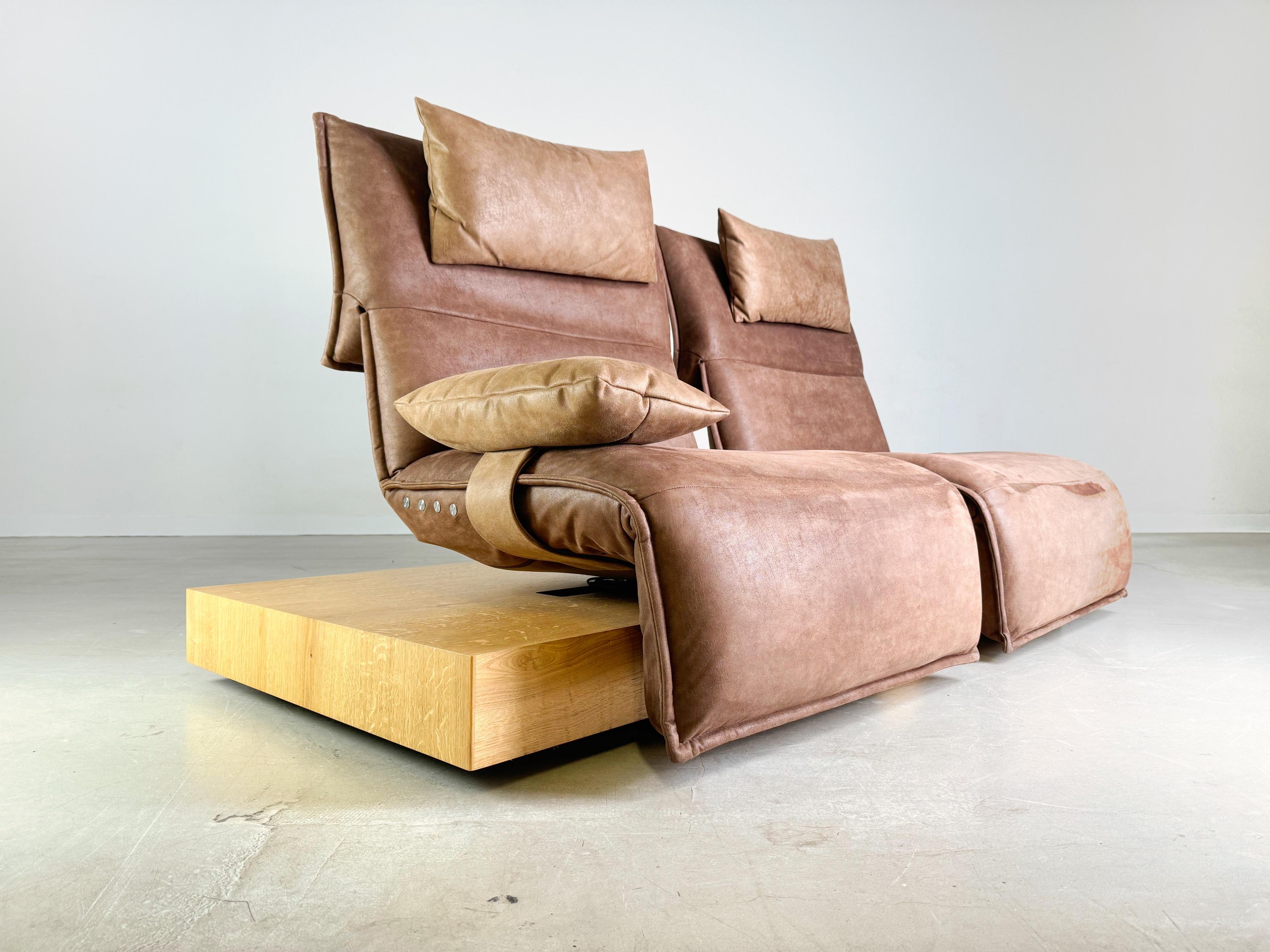 We are offering a beautiful two-seater Edit 3 sofa from Koinor for sale. The seats upholstered in brown suede can be rotated on their own axis and their seating position can also be varied by adjusting the footrests and backrest continuously at the