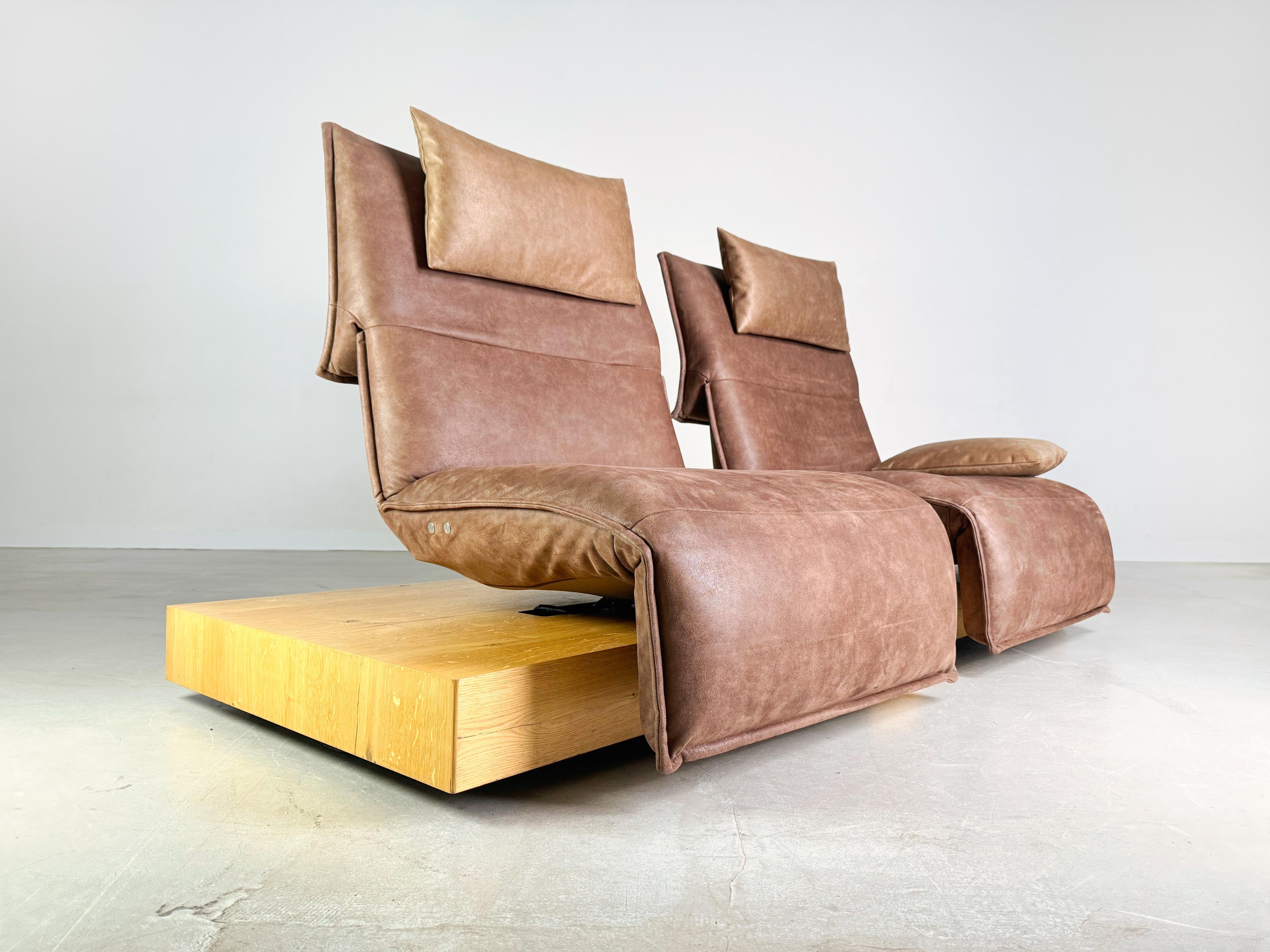 We are offering a beautiful two-seater Edit 3 sofa from Koinor for sale. The seats upholstered in brown suede can be rotated on their own axis and their seating position can also be varied by adjusting the footrests and backrest continuously at the
