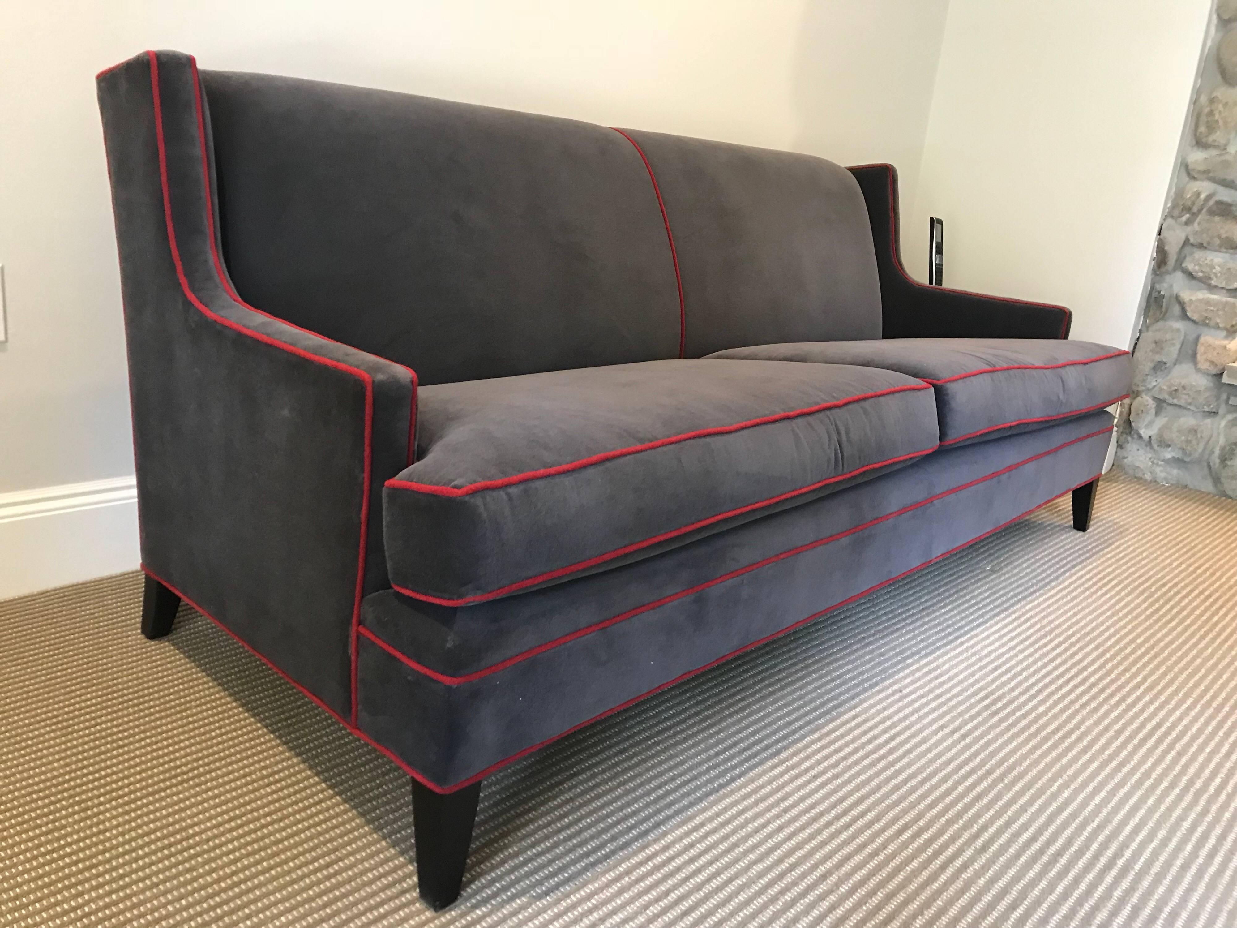 This sofa was manufactured by Mitchell Gold and is covered in dark grey cotton velvet accented with red gimp. It can be purchased with a pair of lounge chairs that match.