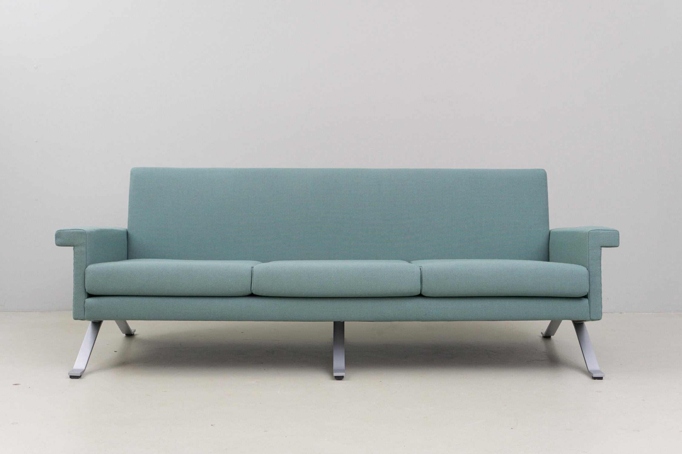 This minimalistic and elegant three-seater sofa has a matt chromed metal structure and new upholstery and cover. The cover is made of 100% wool in a cool grayish green. Excellent condition. 
The last production of this piece was manufactured in