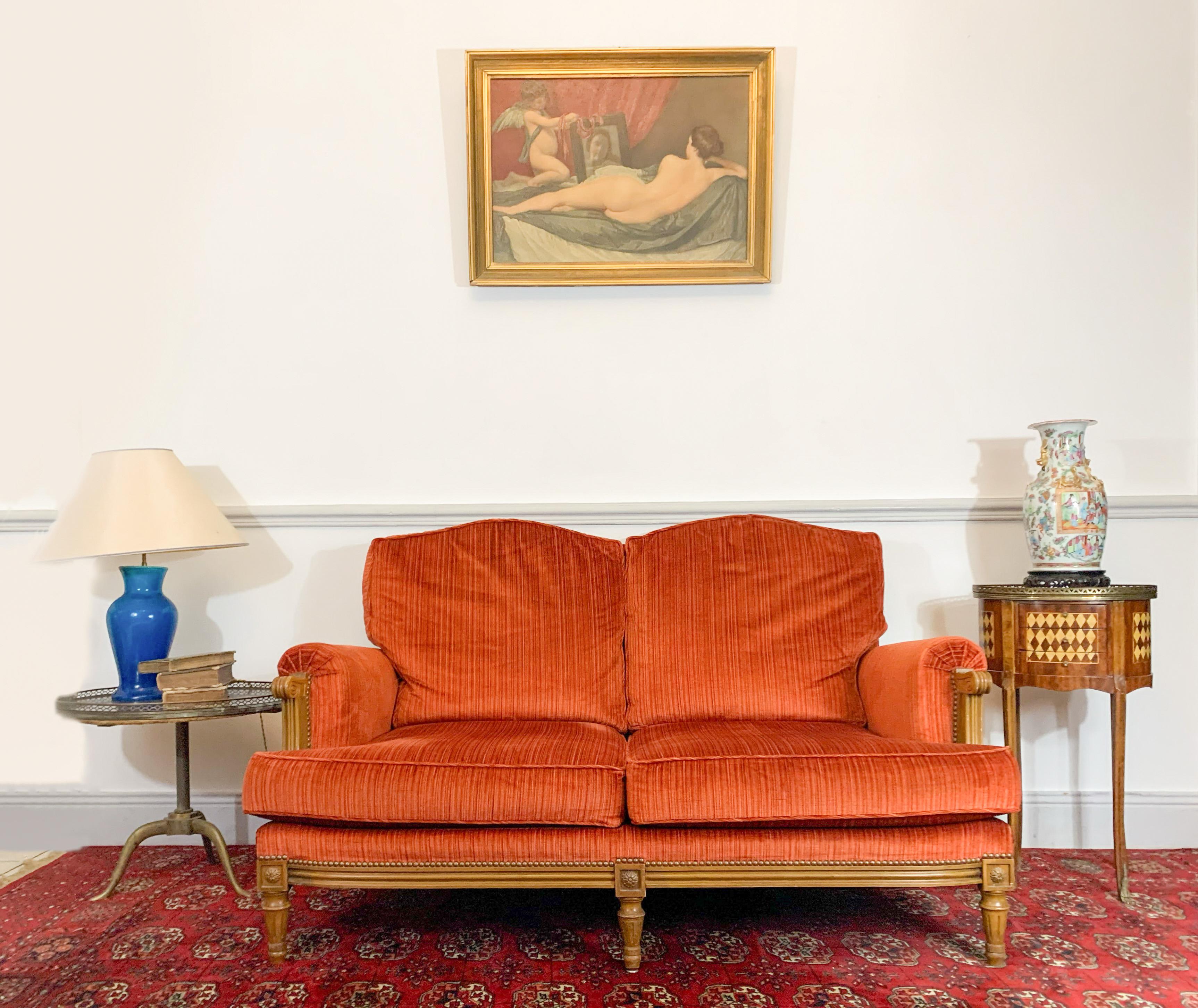 Joli canapé deux places de style Louis XVI. La base du carquois est cannelée. Des motifs floraux sont présents sur les dés de liaison. Les accoudoirs sont en forme de volutes. L'ensemble est recouvert de velours côtelé orange. 
2Oème siècle.