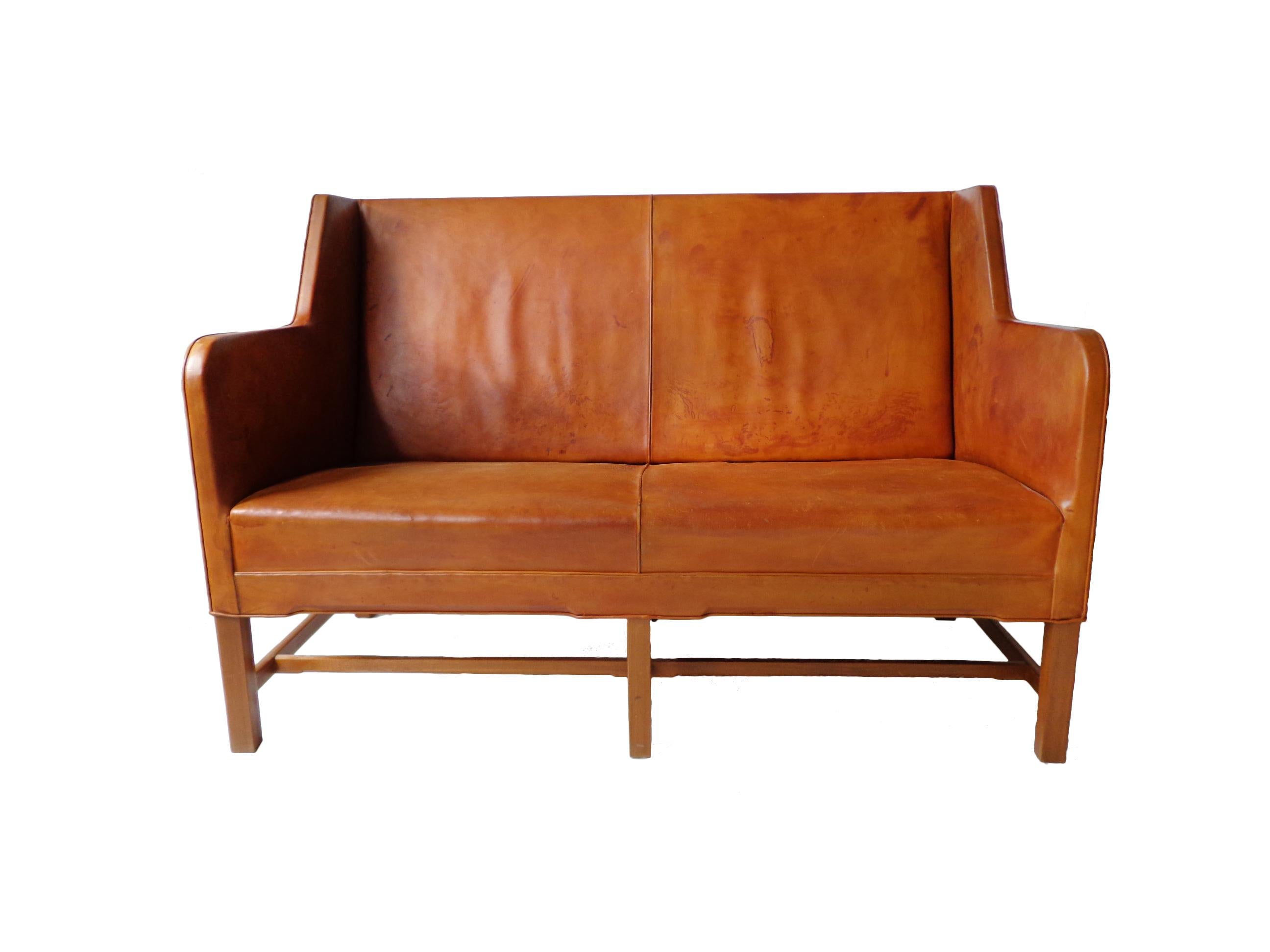 Two-seater sofa model 5011 in original cognac leather and six-legged mahogany base. Produced by Rud. Rasmussen Cabinetmakers, Denmark. Minor marks on the frame, patina to the leather. Back covered in original canvas.
Shown at the Copenhagen