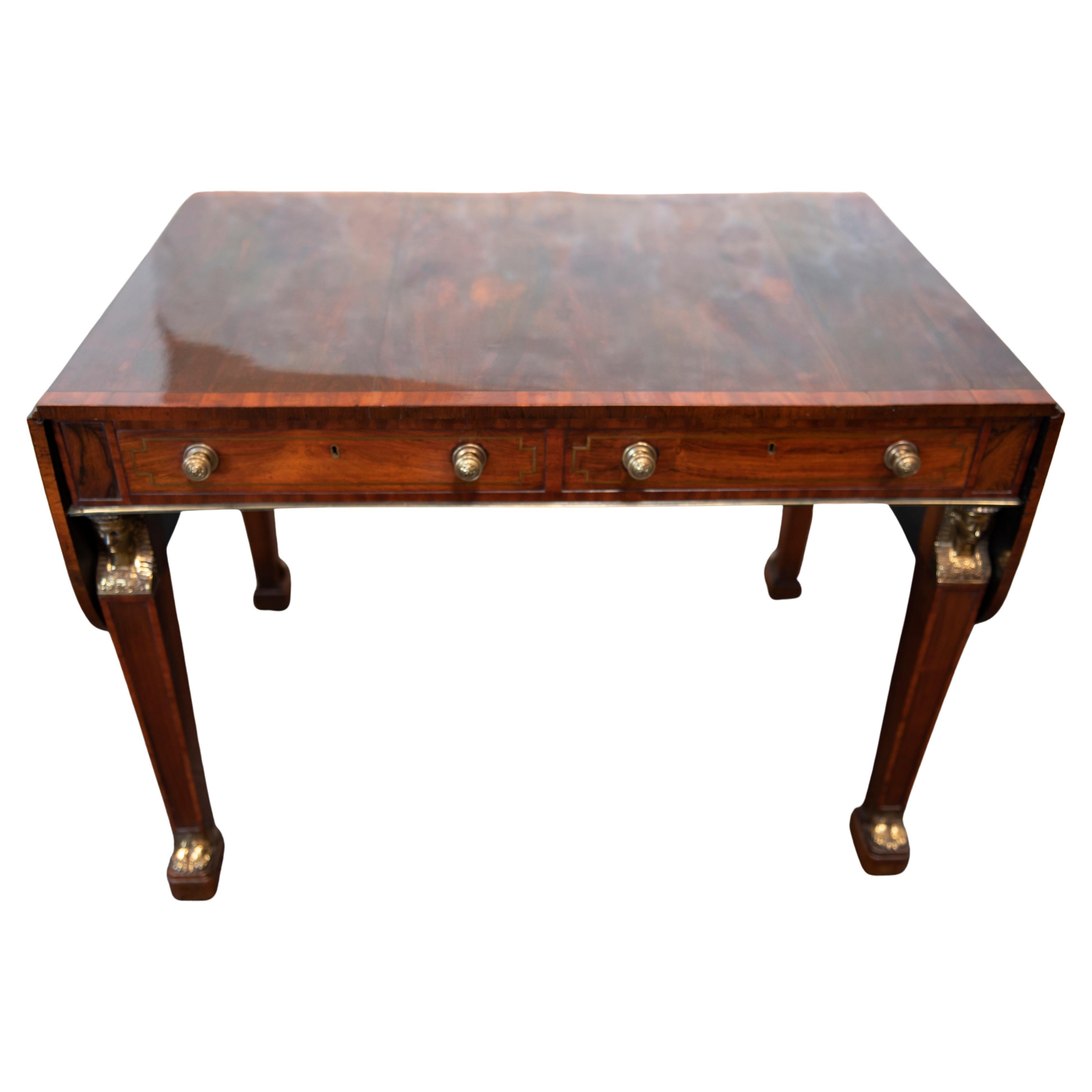 George III Regency period mahogany sofa table in the manner of Thomas Chippendale the Younger. The rounded rectangular twin flap top cross banded in satinwood with two cedar lined frieze drawers inlaid with brass stringing on gilt metal mounted