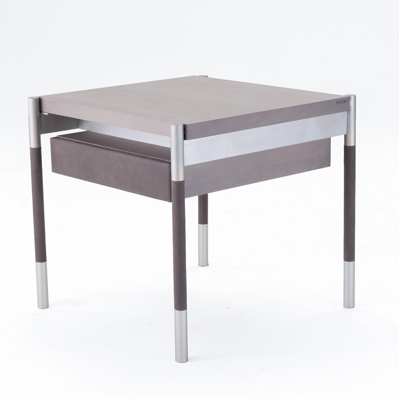 This square coffee table features a maple wood top in light gray, along with a satin anodized aluminum structure in champagne. Its legs are in matching champagne-colored satin anodized aluminum with genuine leather detailing. For added convenience,