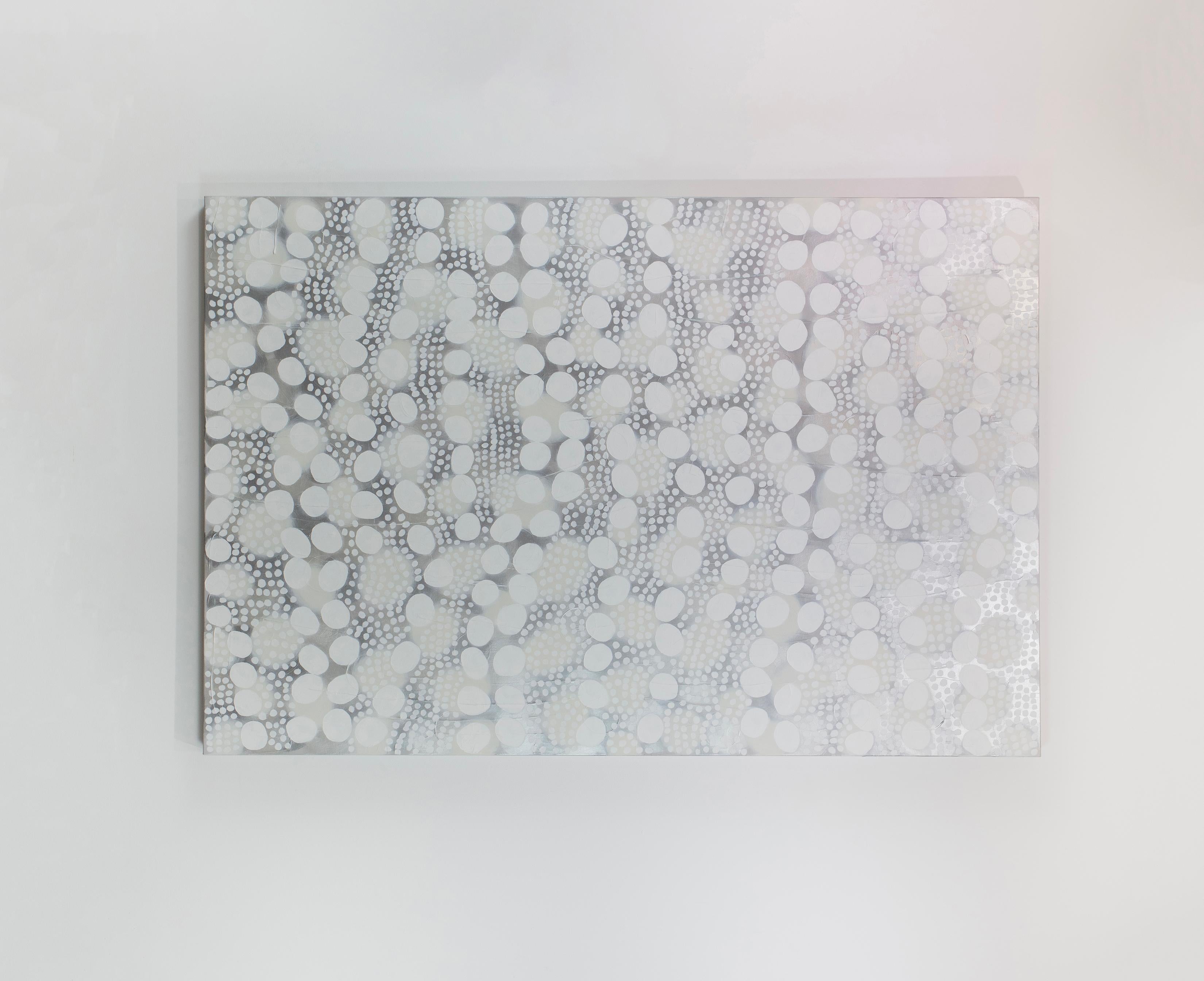 Ce grand tableau abstrait de Sofie Swann présente une palette de blanc et de gris clair, avec des formes circulaires blanches imparfaites de différentes tailles disposées avec de subtils accents métalliques argentés sur toute la toile. Cette
