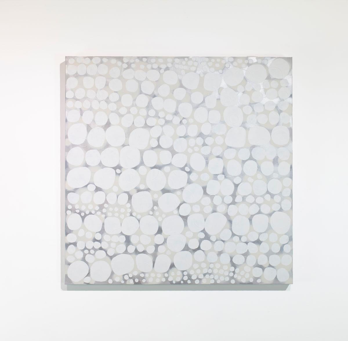 This large abstract painting by Sofie Swann features a light neutral palette, with white circular shapes layered over a hazy grey and cream-colored, subtly metallic background. This painting is made on gallery wrapped canvas with painted sides. It