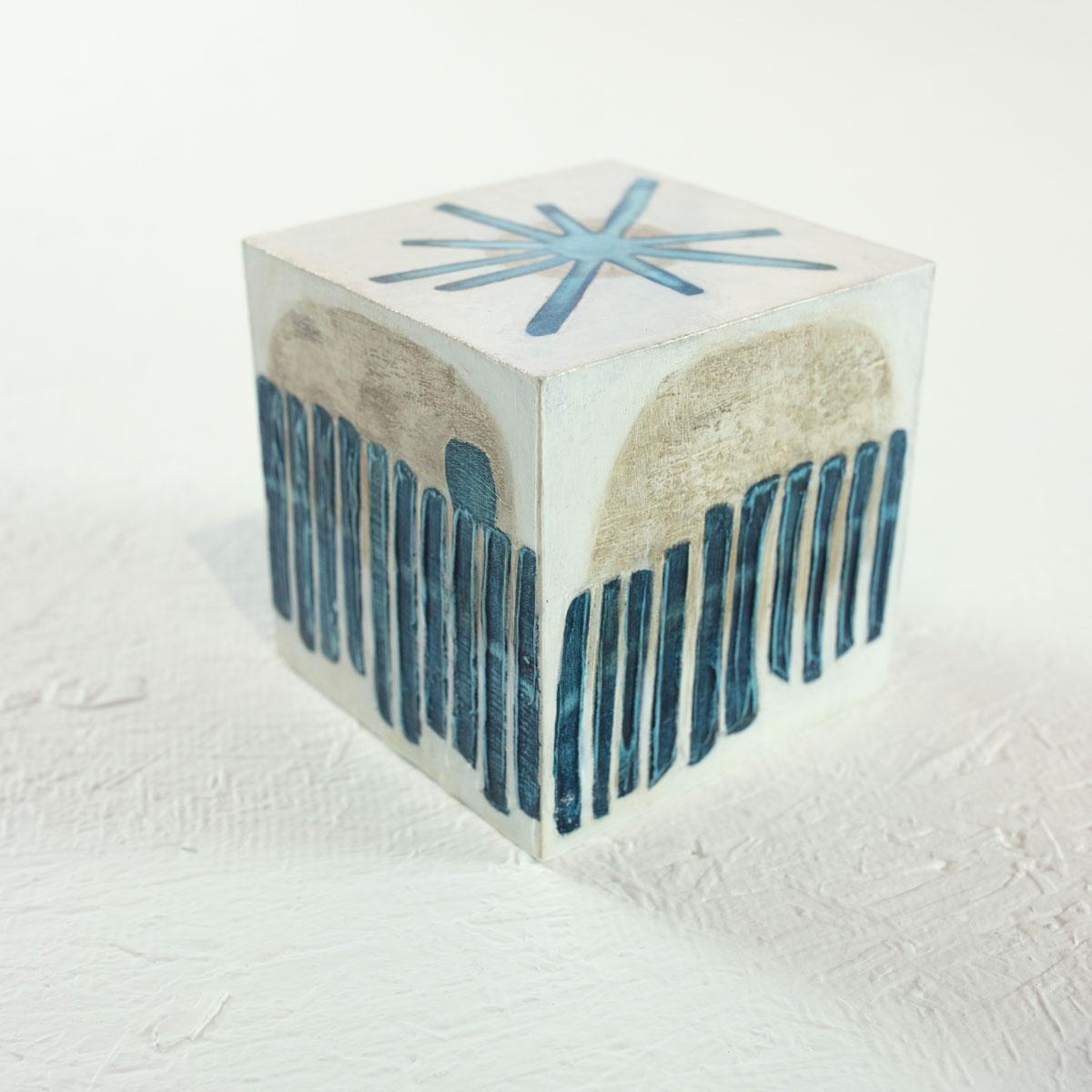 This 4" hand-painted sculptural cube by Sofie Swann is made with acrylic paint and gesso on wood. It features a coastal blue, beige, and white palette, with organic forms and shapes, and light texture on the surface of the cube. It is signed by the