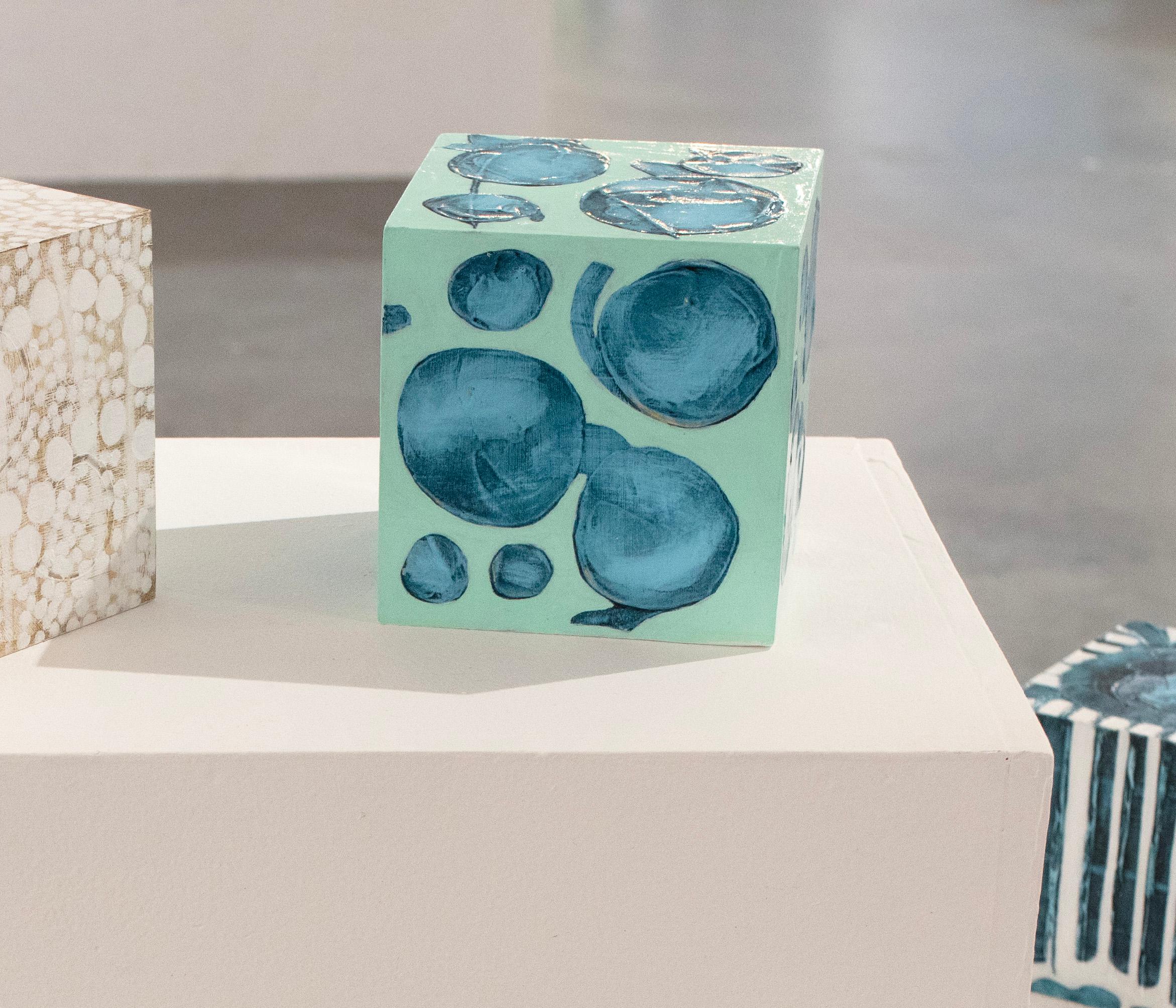 Ce cube sculptural de 5 pouces peint à la main par Sofie Swann est réalisé avec de la peinture acrylique et du gesso sur bois. Il présente une palette froide avec un fond vert turquoise et des formes circulaires sarcelles peintes sur la surface. Il