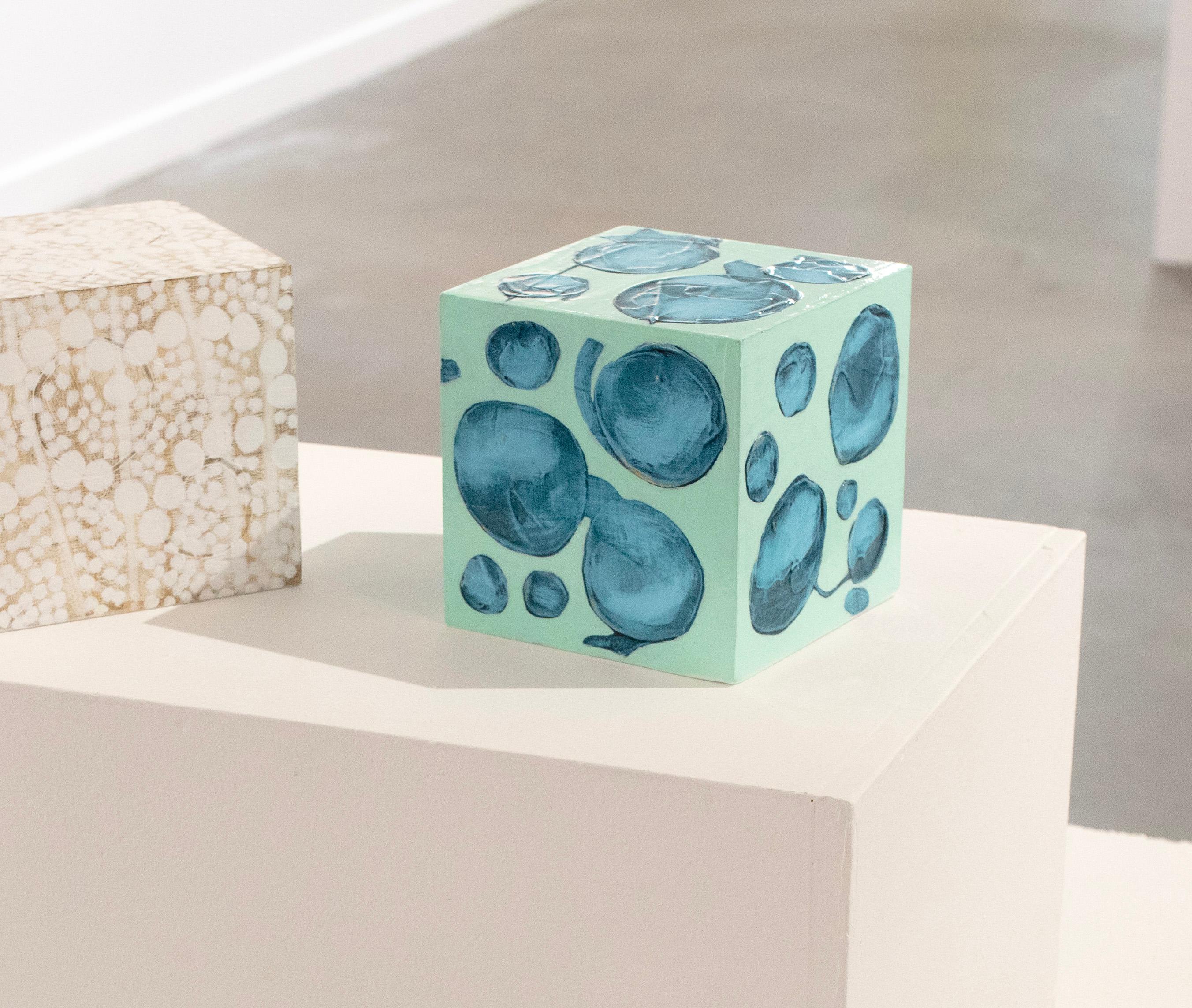 Questo cubo scultoreo di 5 pollici dipinto a mano da Sofie Swann è realizzato con colori acrilici e gesso su legno. Presenta una tavolozza fresca con uno sfondo verde turchese e forme circolari dipinte in verde acqua sulla superficie. È firmato