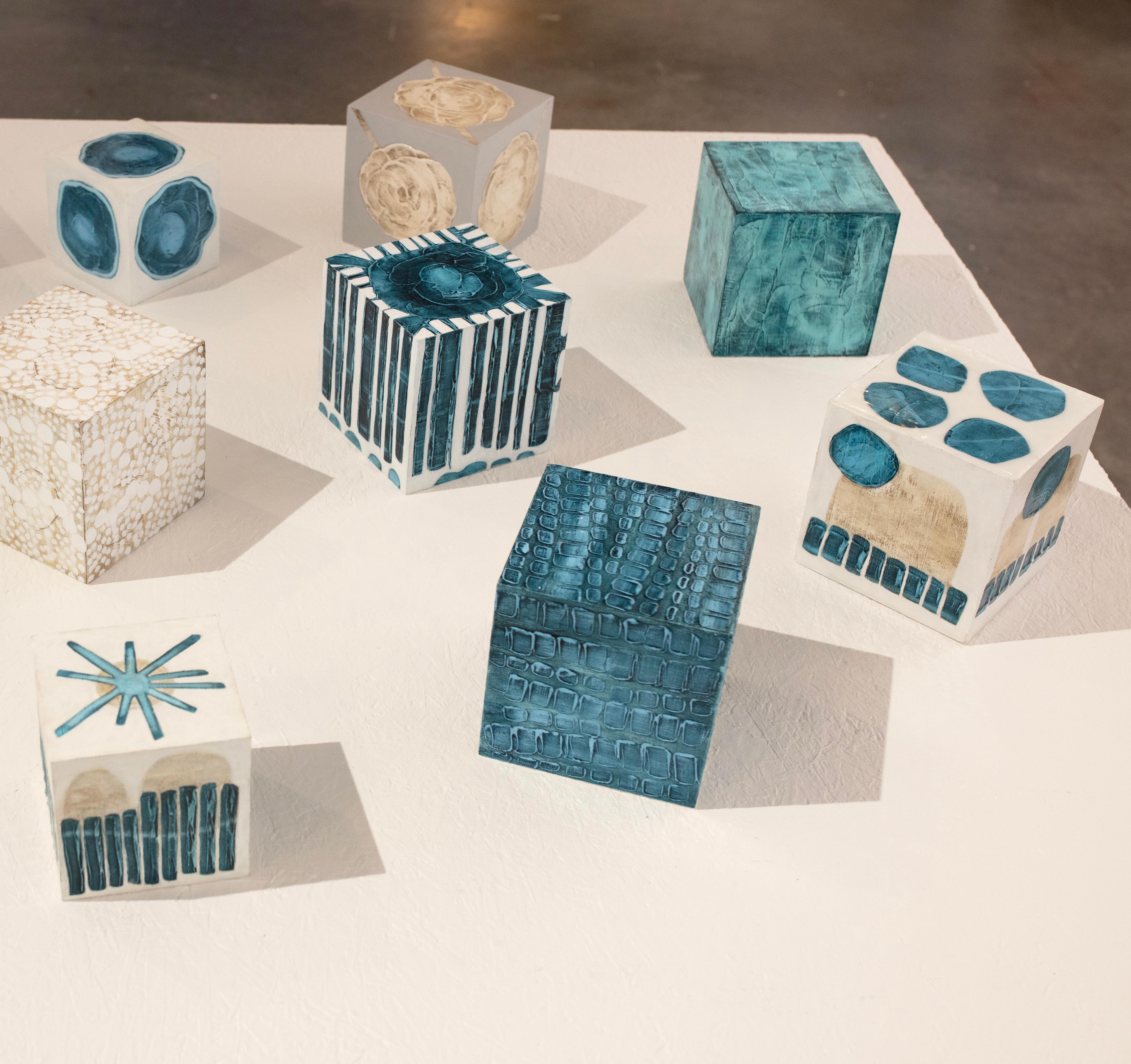 Ce cube sculptural de 5 pouces peint à la main par Sofie Swann est réalisé avec de la peinture acrylique et du gesso sur bois. Elle présente une palette de sarcelles profondes avec des formes rectangulaires légèrement texturées gravées dans la
