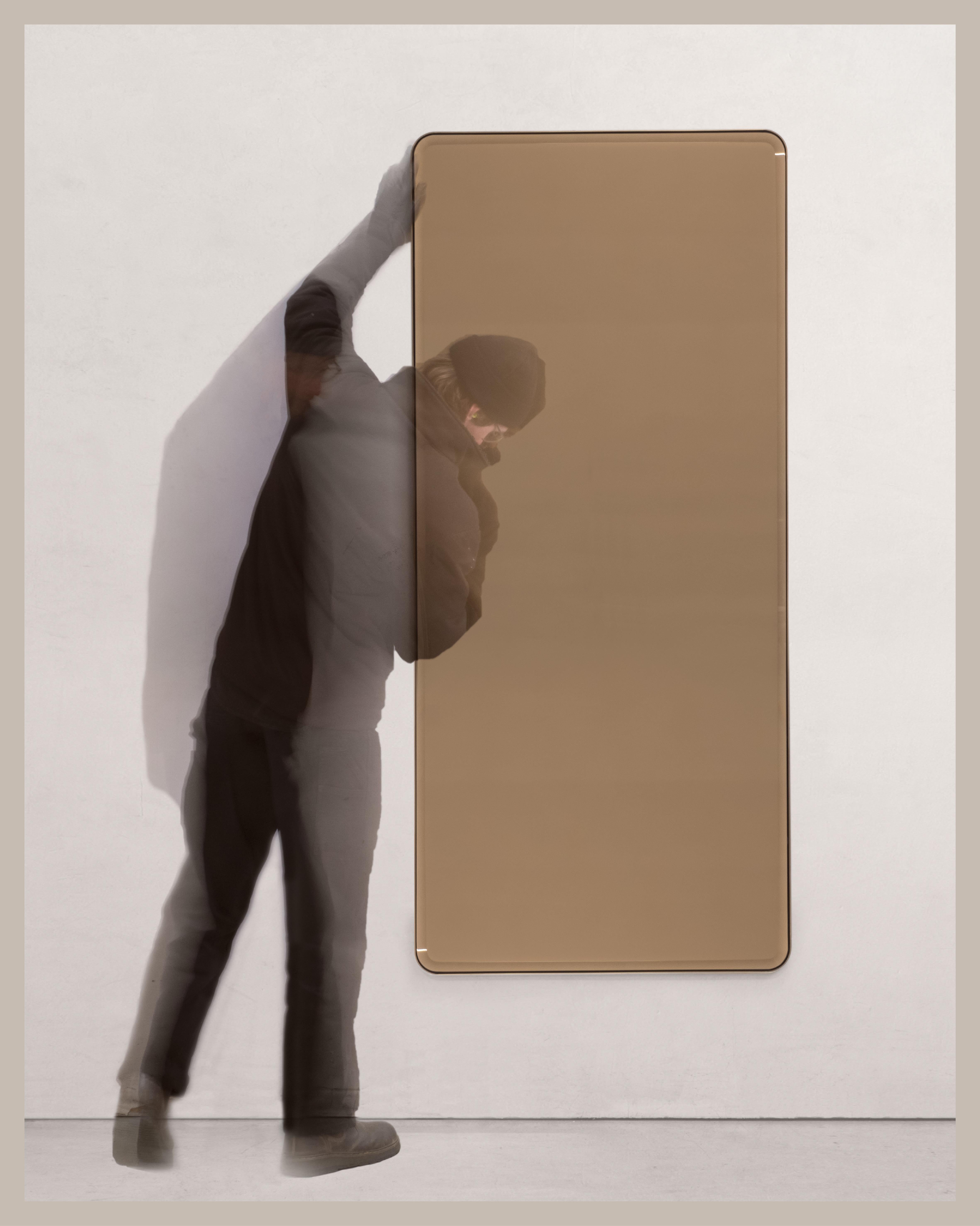A wall mirror with bevelled glass mirror. Various metal, finish and mirror tint options are available. Hand crafted in the North to order.

Initial image shows a polished brass frame with bronze tinted mirror.