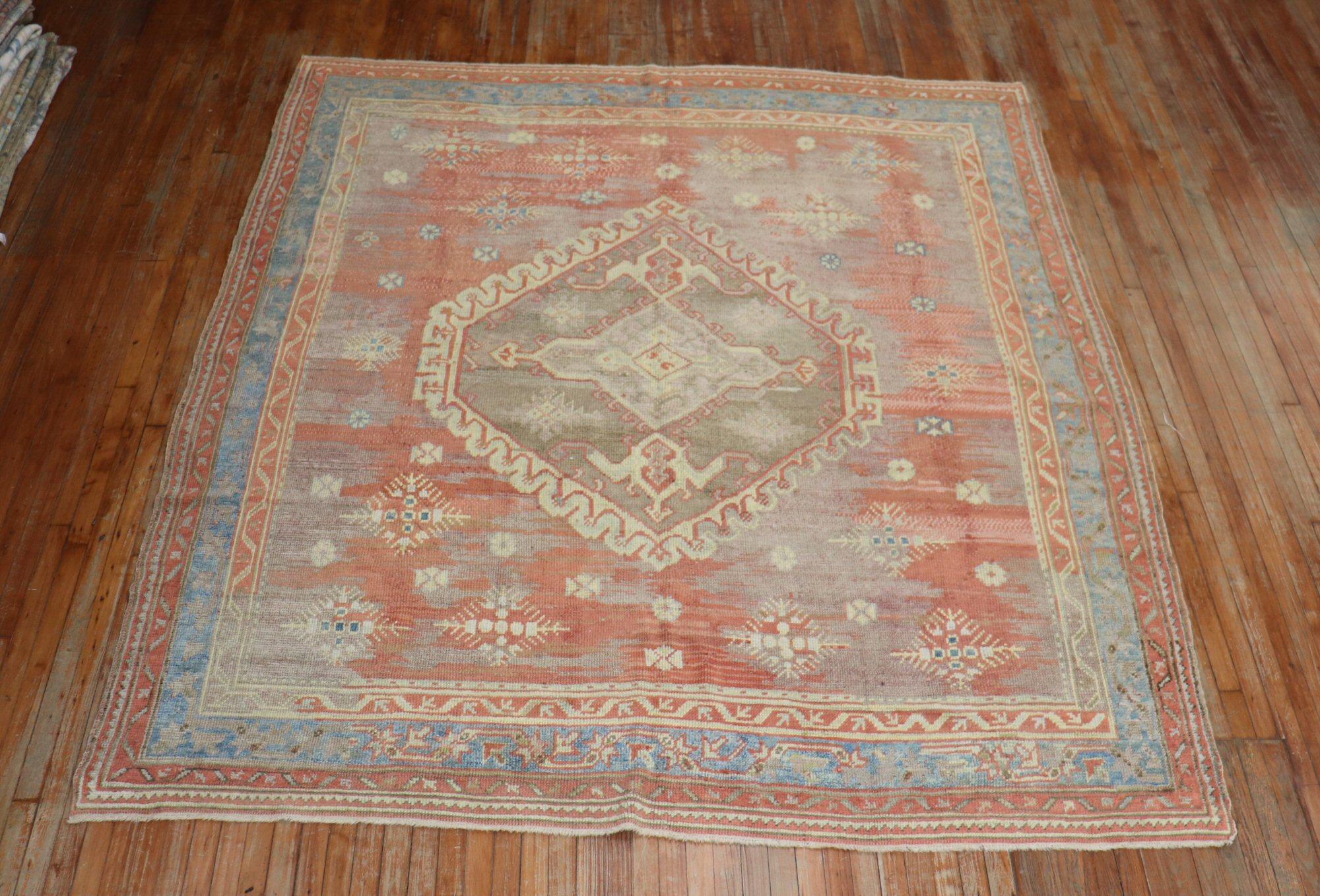 Square-shaped one-of-a-kind Turkish Oushak rug with a large scale medallion on a muted red ground and multi-band border. Accents colors in yellow, green, and blue. The Brown areas in the field are not worn areas, they are different colored undyed