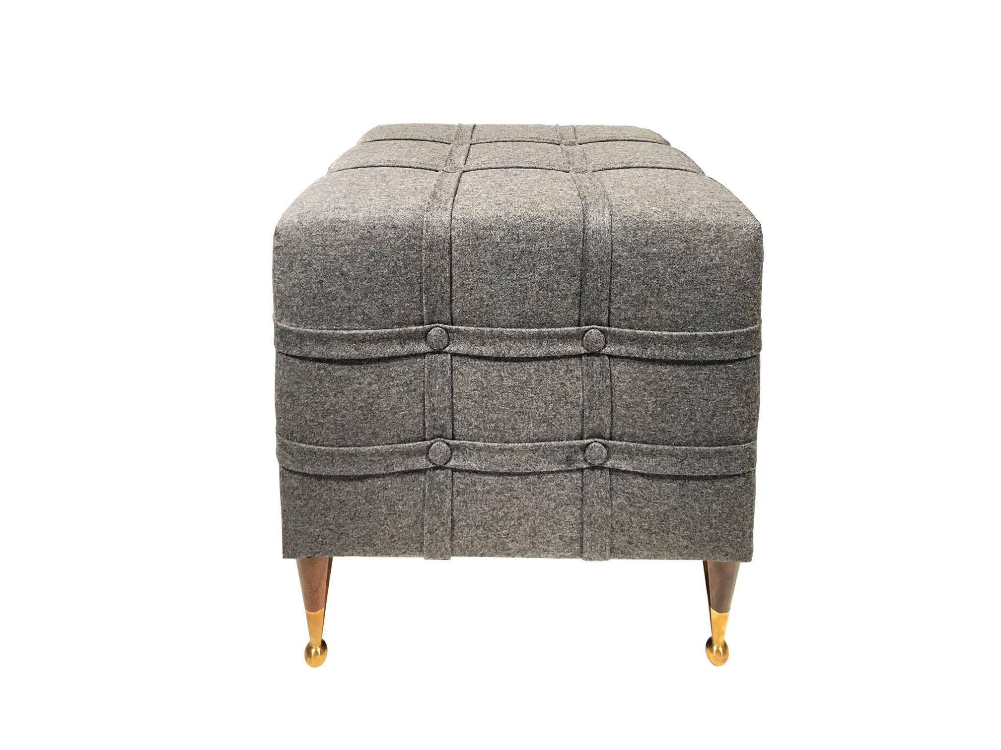 The Soho Claremont Ottoman, designed by Irwin Feld for CF MODERN, has a plush cushion wrapped in four straps with button details. The cushion stands on four cone shaped Claremont legs with brass sabots. Shown here in grey flannel.

CF MODERN