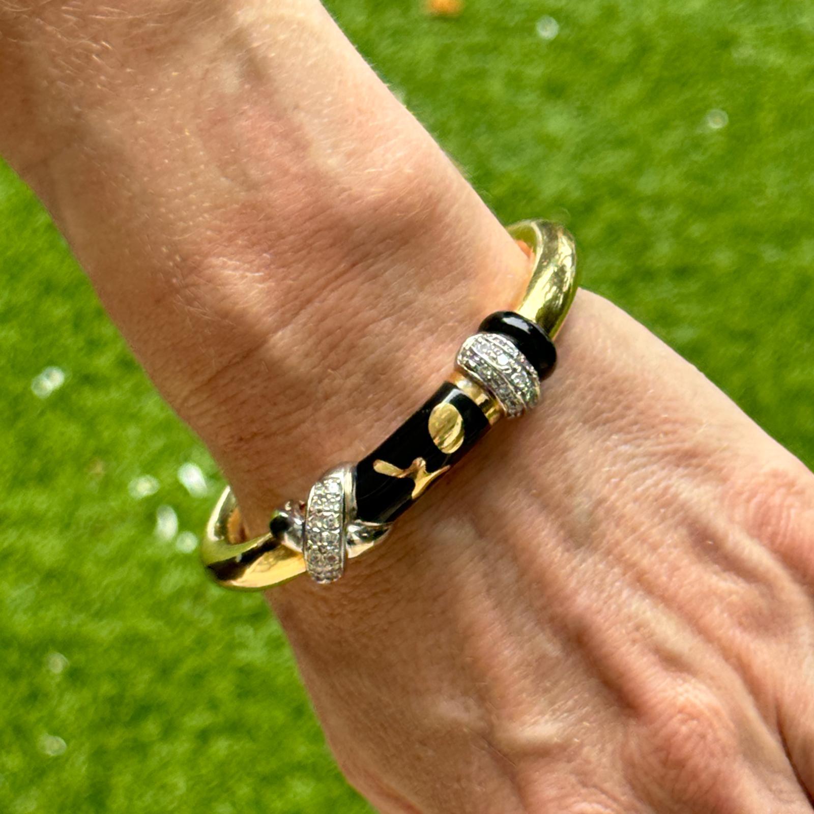This SOHO Italian Diamond 'X' and Black Enamel Hinged Bangle Bracelet is a luxurious and modern piece, crafted from 18K Yellow Gold. Measuring 9mm in width, the bangle features a sleek design with bold black enamel acceents that contrast elegantly
