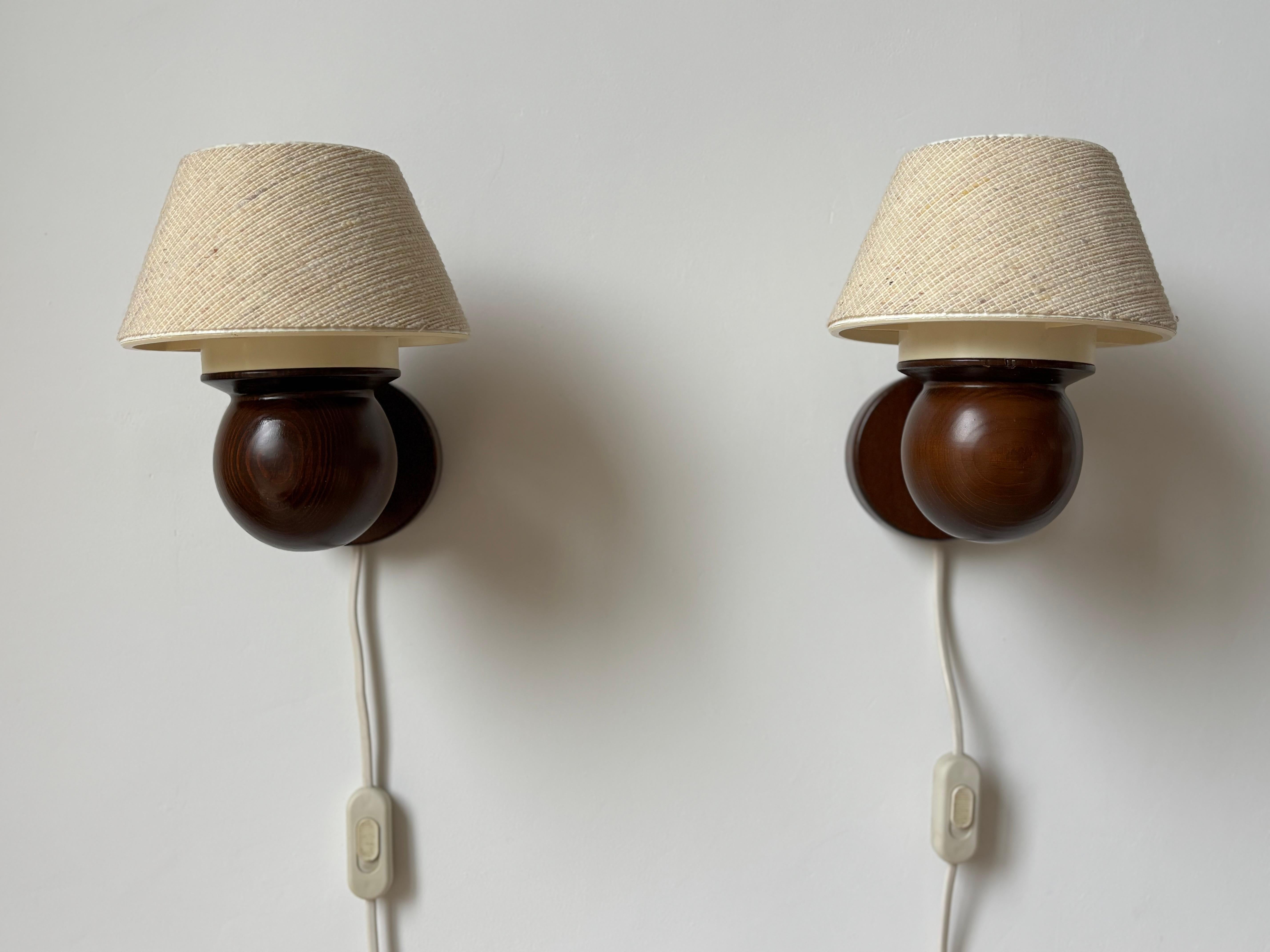 Pair of lacquered pine wood wall lights produced by Solbackens Svarveri in Sweden in the 1970s. Warm dark brown wooden lamps with original sand beige colored textile tapered drum shaped shades. 
Fitting for E27 bulb. Switch on cord. 
Great vintage