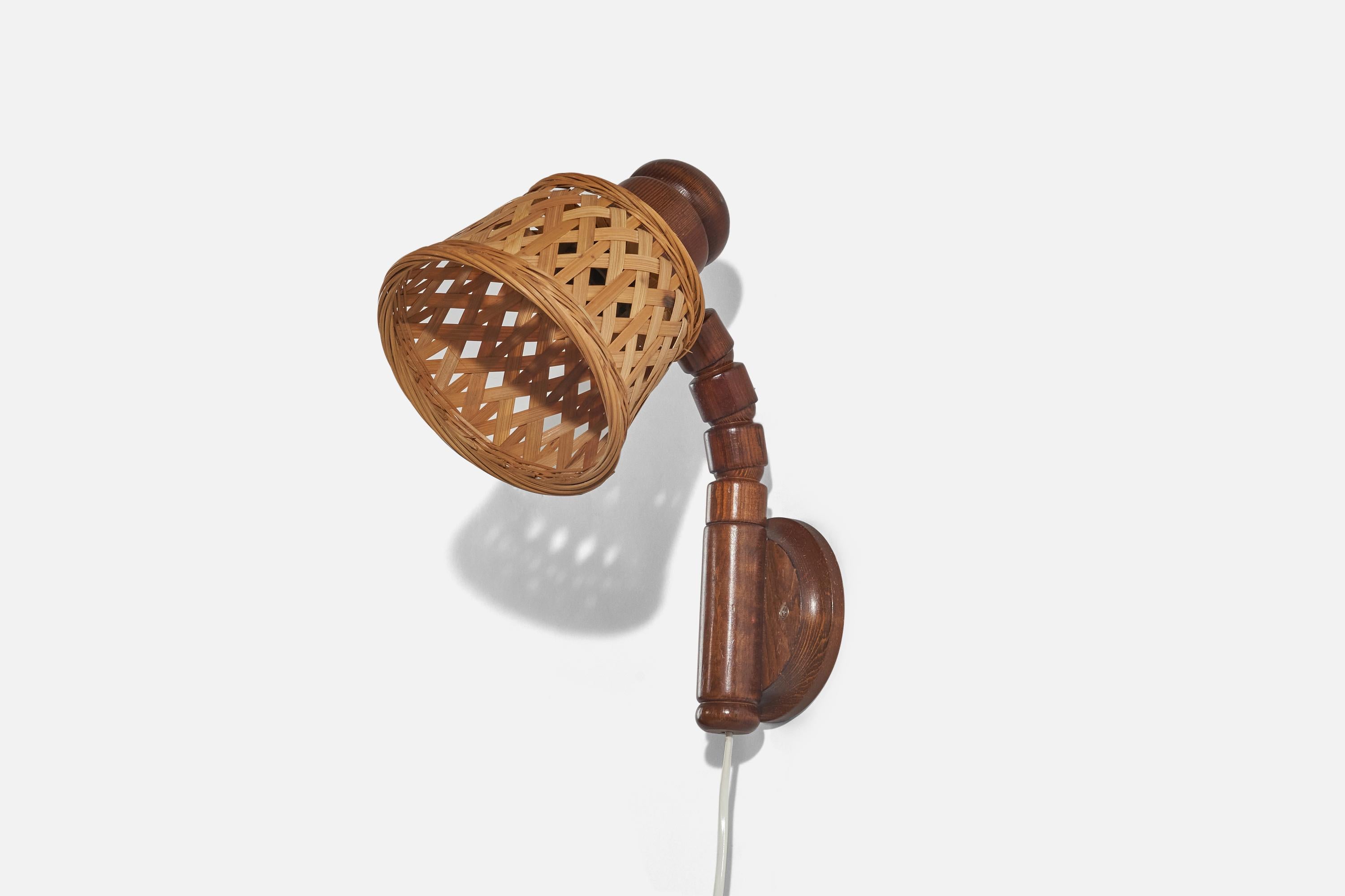 A pine and rattan wall light designed and produced by Solbackens Svarveri, Sweden, c. 1970s. 

Sold with Lampshade. 
Stated dimensions refer to the Sconce with the Shade. 
Variable dimensions, measured as illustrated in the first