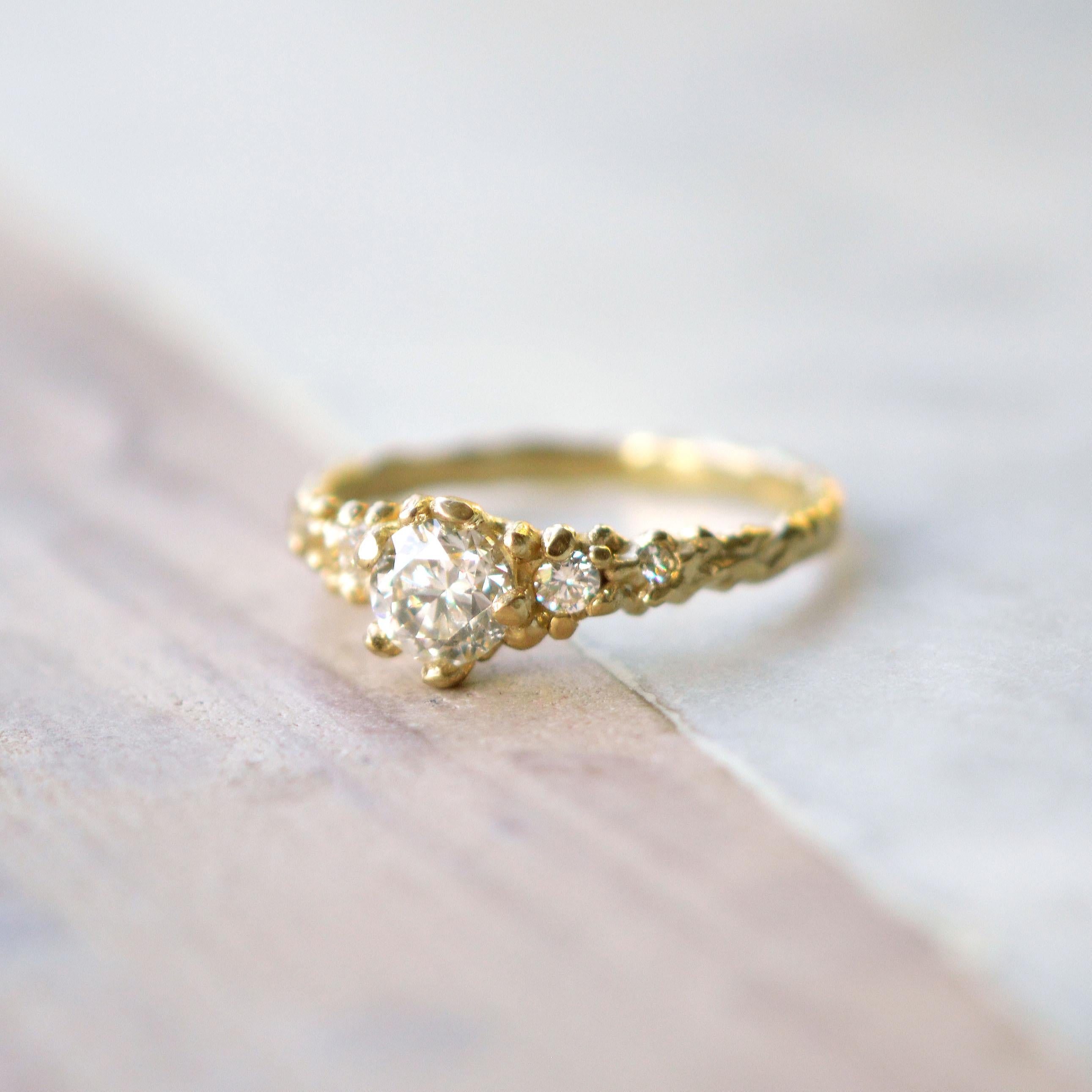 This charming ring has an 18ct gold earth inspired setting and includes a central 0.8ct antique cut ethically sourced diamond, with four brilliant cut accent diamonds on either side. This piece was created from Lucy's original hand-sculpted