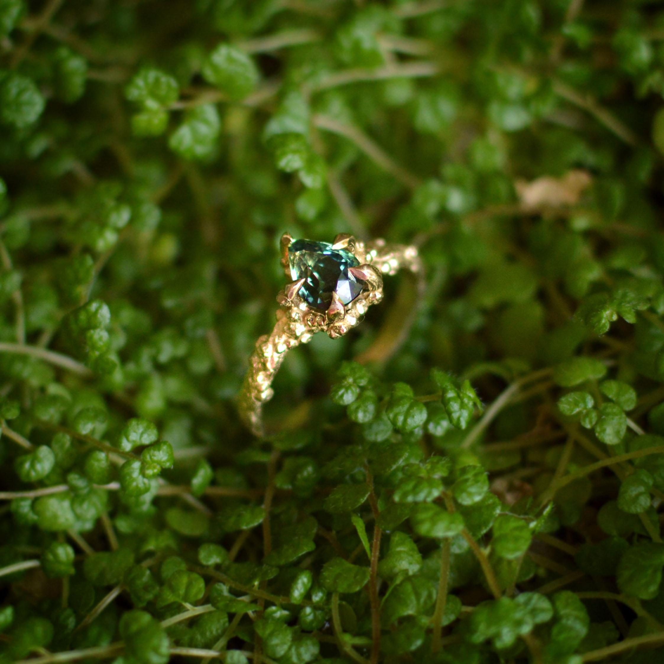 Dieser magische, vom Ozean inspirierte Ring ist mit einem 1,1 ct. natürlichen, blaugrünen Montana-Saphir in einem wunderschönen, champagnergelben 9-karätigen Goldband besetzt.  Dieses Stück wurde nach Lucys originalem, handgeformten Entwurf