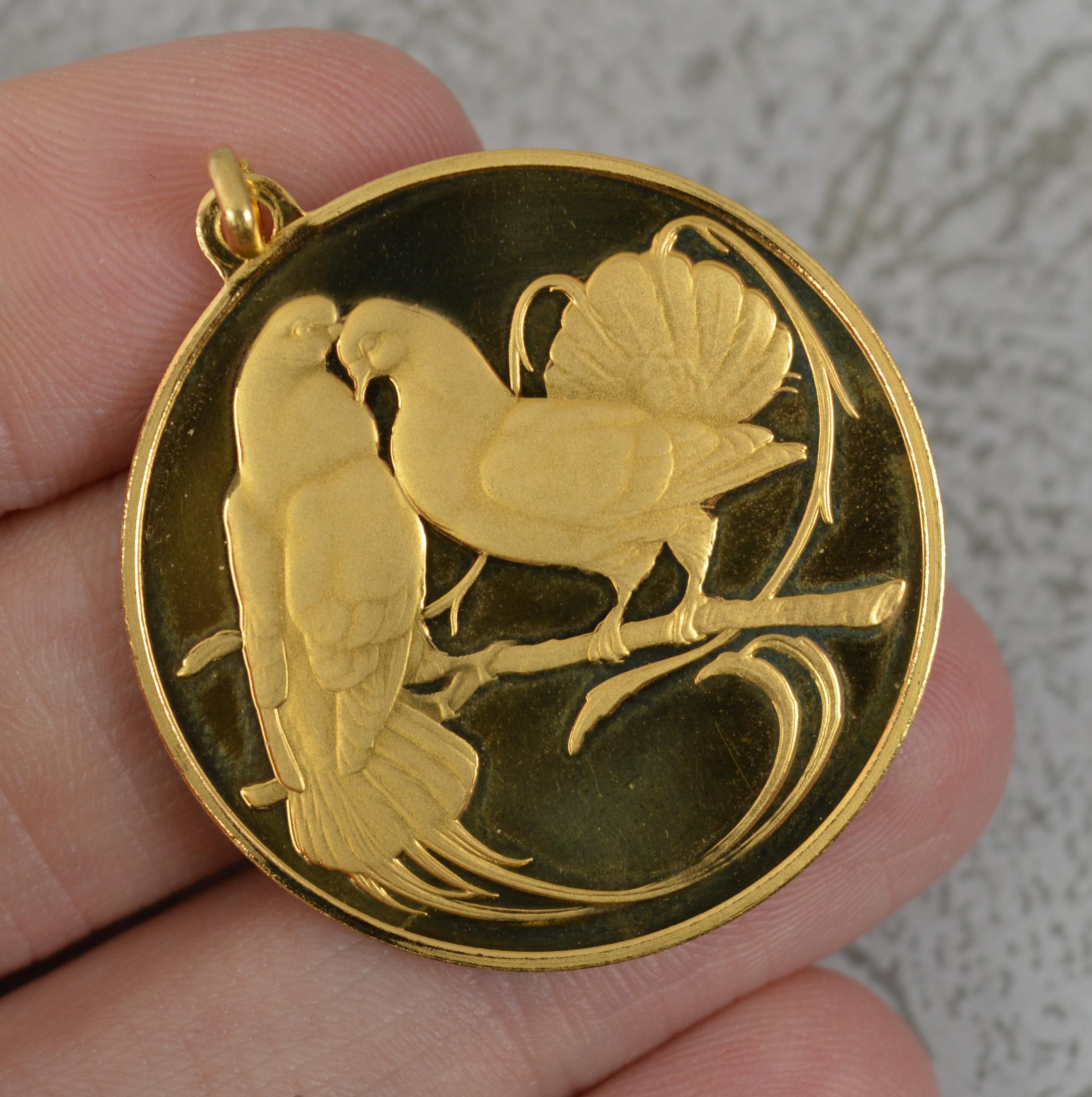 A superb contemporary circular pendant medal. 
Solid 18 carat yellow gold example.
Designed with two turtle doves to front, polished reverse and matt birds. To the reverse is the French phrase 'Ni vous sans moi, ni moi sans vous' which translatess