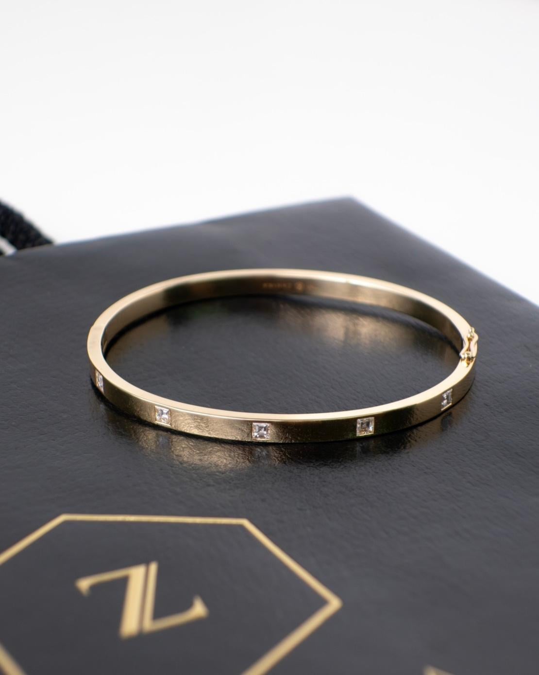 Fabriqué en or jaune 18 carats massif, cet élégant bracelet présente un design minimaliste mais saisissant avec des diamants naturels de taille carrée dispersés organiquement sur la surface. Chaque diamant est serti avec précision pour capter la
