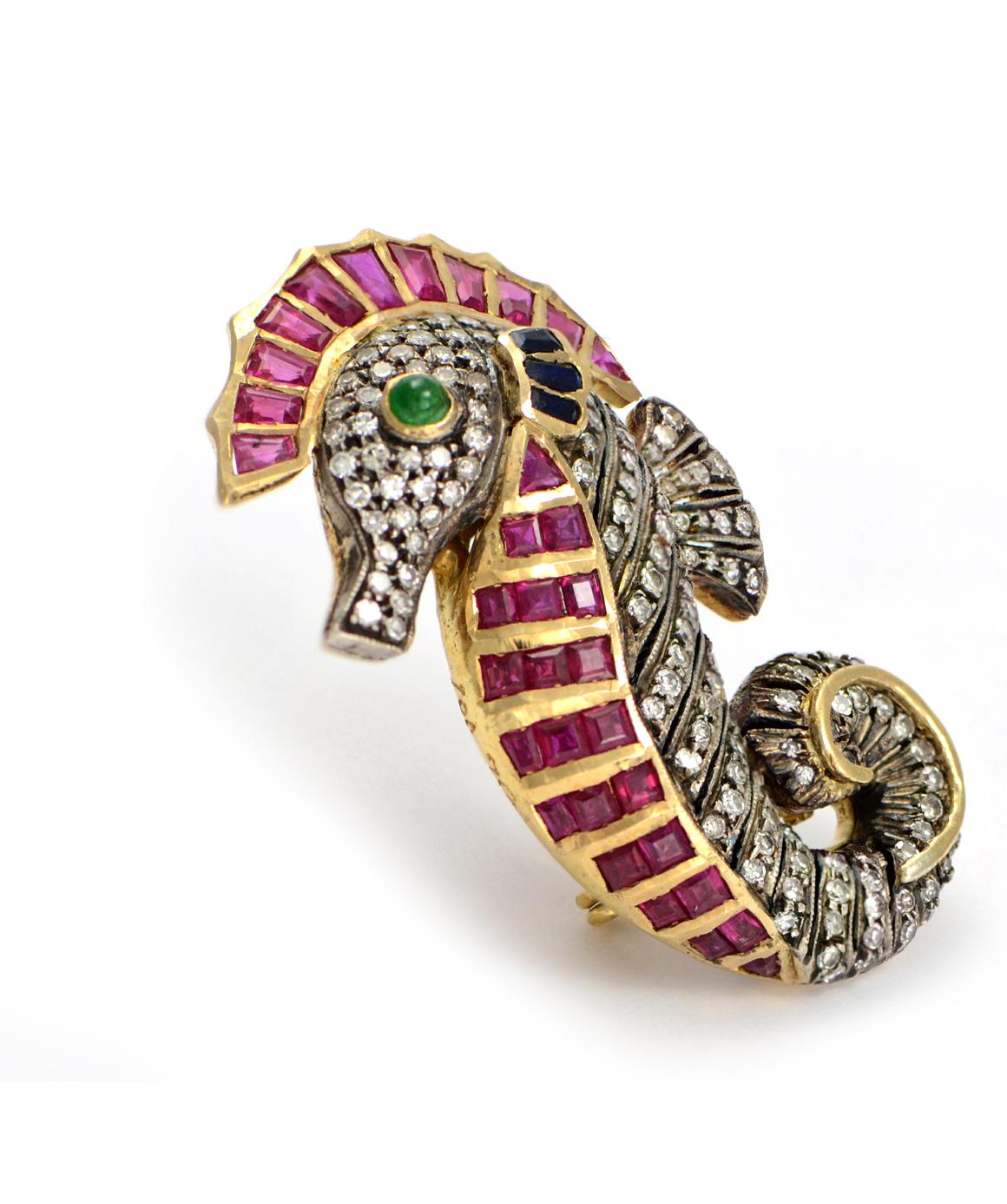 Excellent condition. This cute seahorse brooch is composed of solid 18k yellow gold with sterling over the gold. It features 33 genuine rubies that range from baguettes to square to trillion. There are 3 baguette sapphires and 1 cabochon emerald eye.