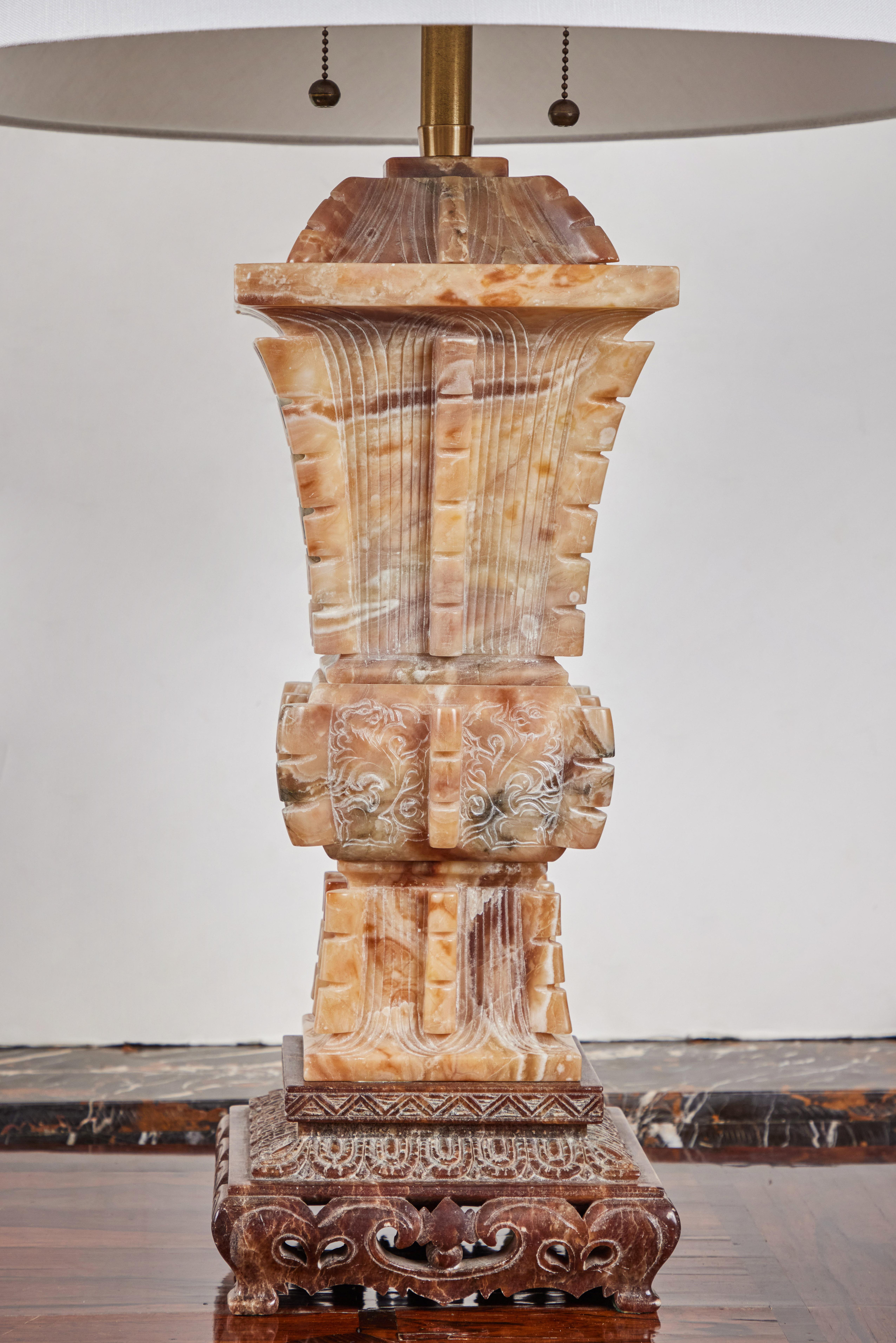 A striking, large, richly carved, solid, golden alabaster, beaker-form table lamp in the Chinese style. The whole surrounded by eight, segmented extrusions and embellished with incised foliate forms, ribbing, and subtle images of dragons . The piece
