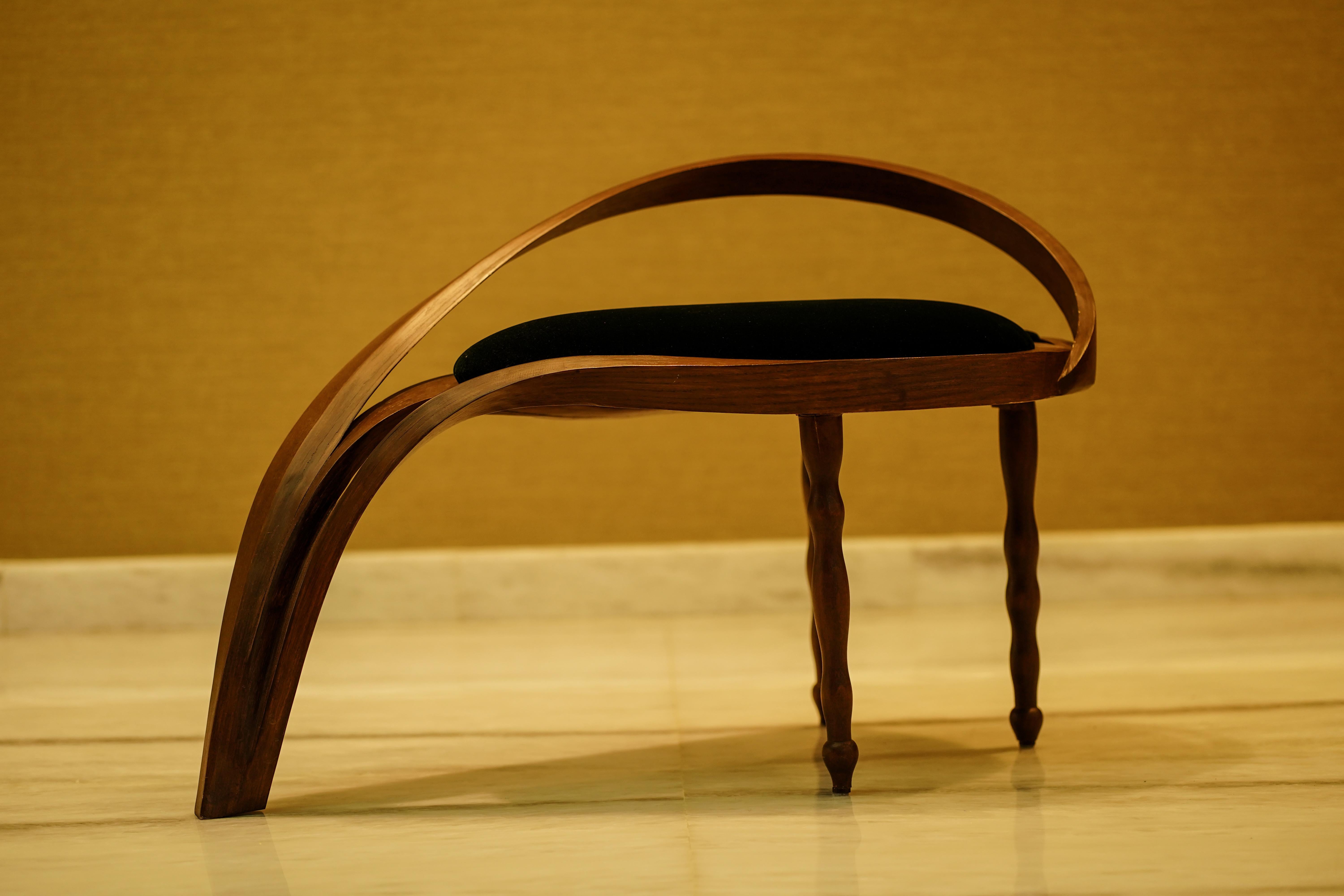 A side/filler chair made in solid ashwood by bending wood. Three of the legs have been made using the wood-turning technique to adopt an abstract natural wave-like design. It has been upholstered in a dark green velvet, in two separate sections. The