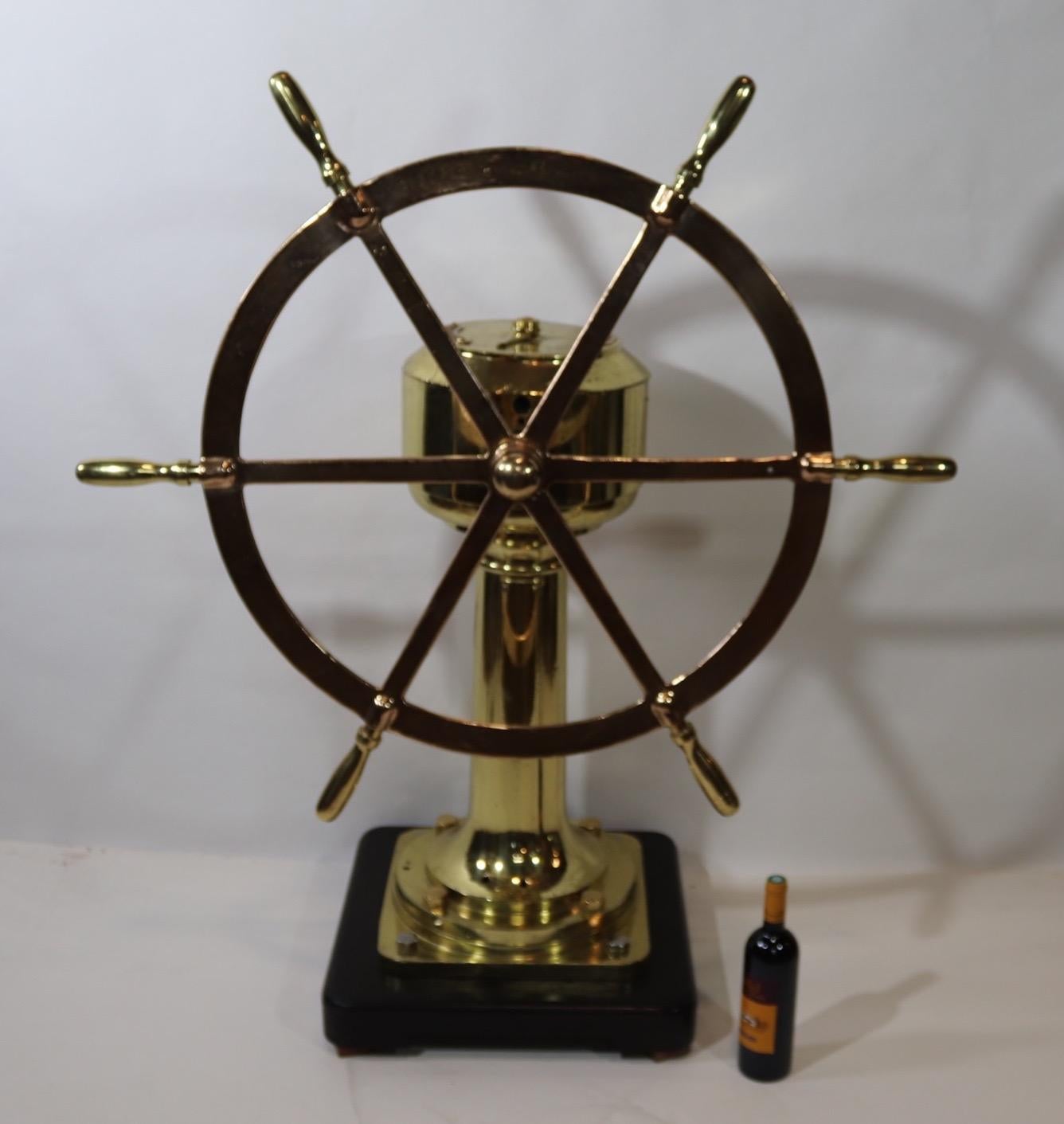 Massive brass pedestal fitted with a six spoke solid brass ships wheel that has been meticulously polished and lacquered. Head of unit has port and starboard plates with indicator arrow driven by internal gears showing rudder angle in degrees.