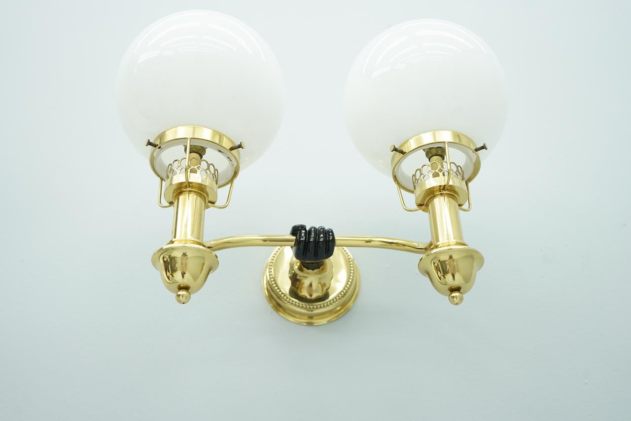 Wall Light in s solid brass with white glass globes by the Vereinigten Werkstätten Munich from the 1970s. A black-lacquered hand holds a latern white glass globe. Each lamp need 2 bulbs with and E14 socket with maximum 40 Watts, or a LED bulb.