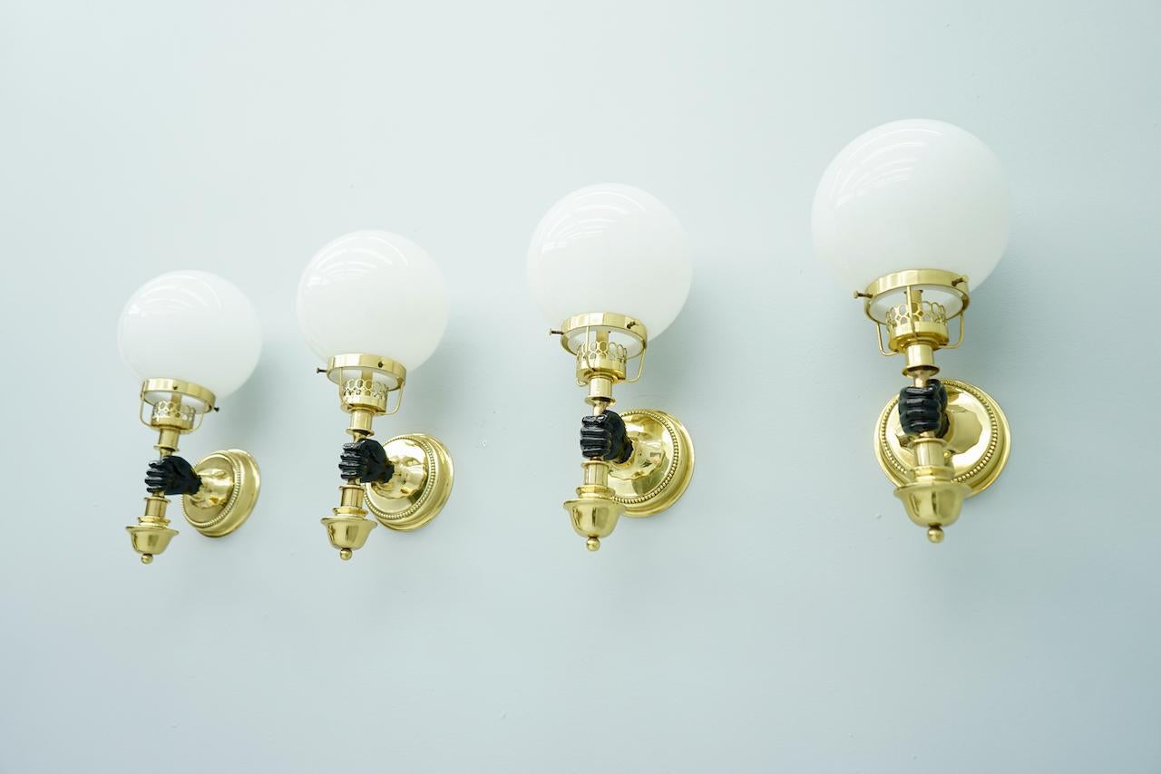 Nice set of wall sconces solid brass with white glass globes by the Vereinigten Werkstätten Munich from the 1970s. A black-lacquered hand holds a latern white glass globe. Each lamp need a bulb with and E14 socket with maximum 40 Watts, or a LED