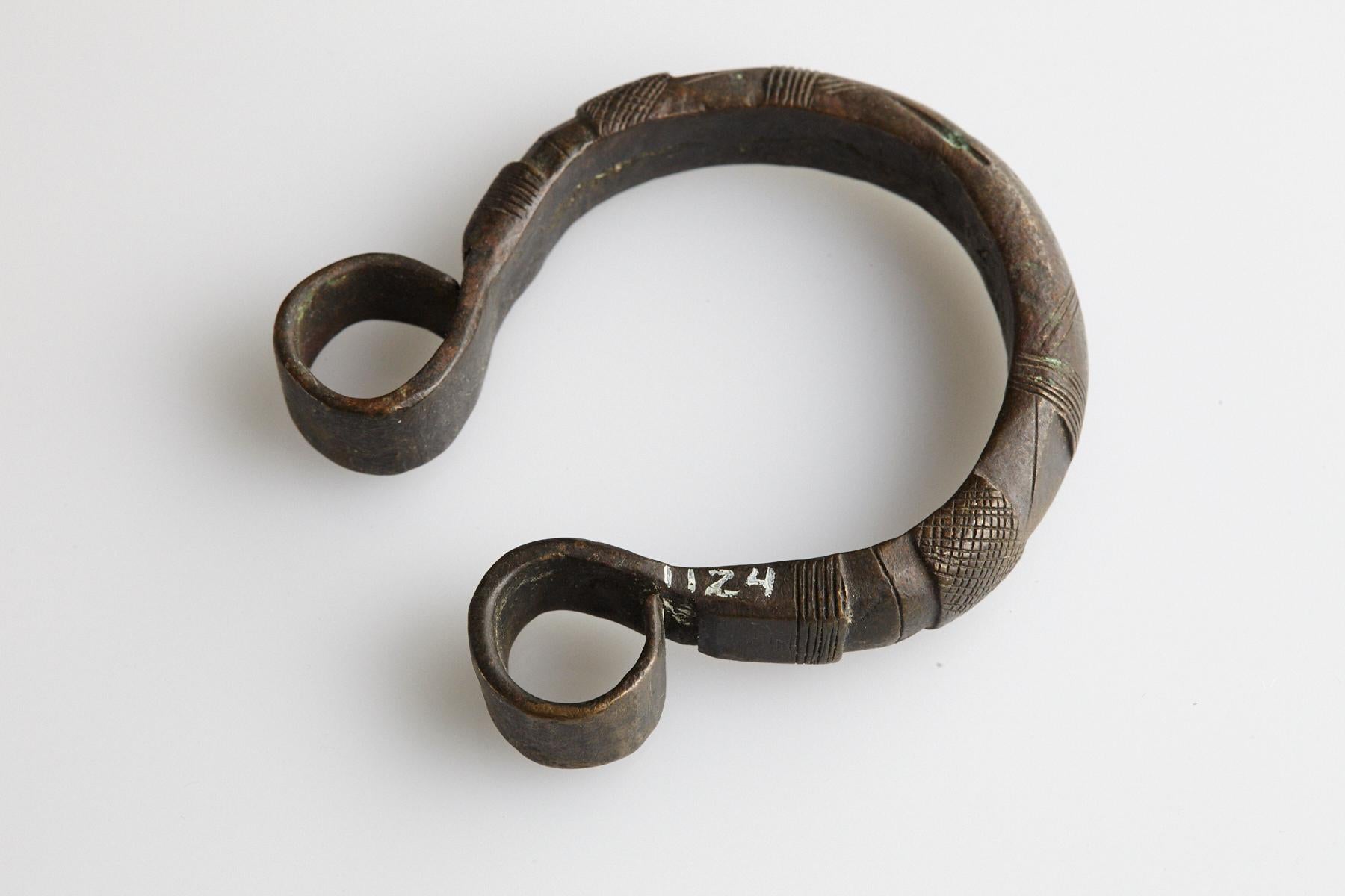 Early 20th-century brass currency bracelet / Manilla in horseshoe form with fixed opening. Hand-stamped and shaped graphical motives and the tips are in the shape of scrolls. This type of bracelet is worn by the Fulani and Gurma People, who are