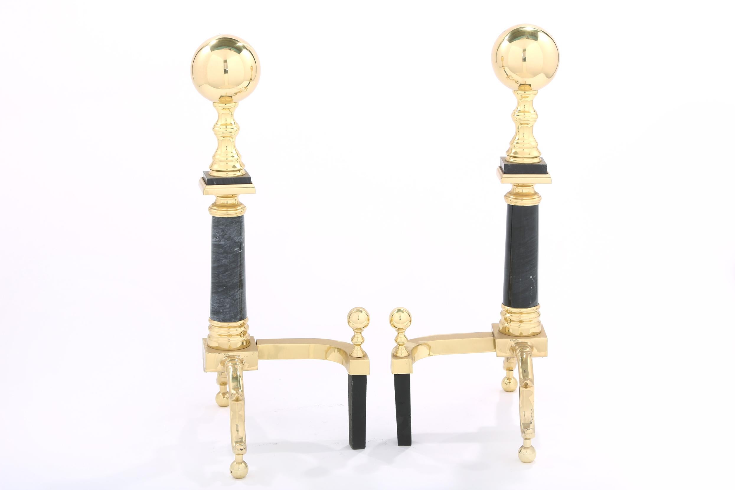 Mid 20th century solid brass with black marble regency style pair of andirons / fireplace accessories with exterior design details. Each one is in good condition. Each one stand about 22 inches high x 13 inches wide x 9 inches deep.