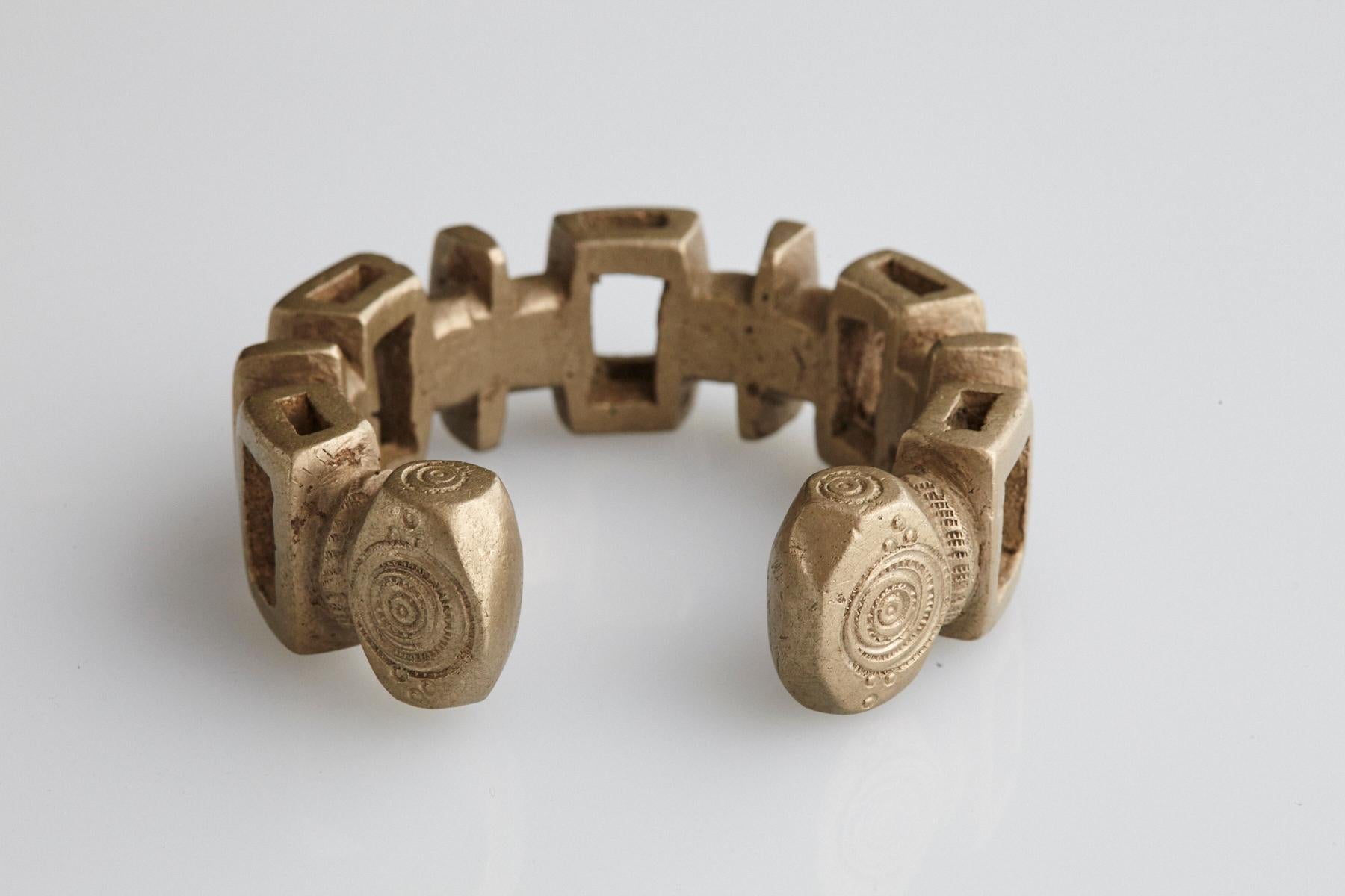 Late 19th or early 20th-century brass or copper alloy with higher nickel content. Bracelet in horseshoe form with fixed opening. Pierced design with rectangular shapes and carved swirling patterns. Nupe People, Nigeria.
170,00 gr / 6.02 oz. Opening