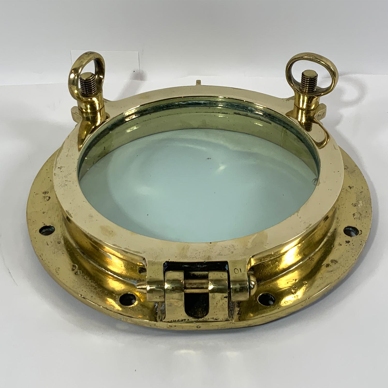 Polished and lacquered ship's porthole with hinged door and two dog bolts. Very Fine finish and clear glass. Circa 1930. Fifteen inch overall.