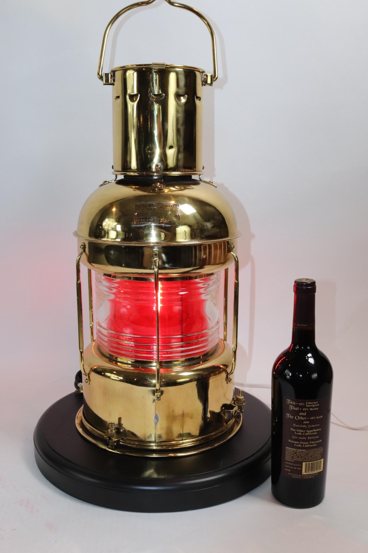 Highly polished ships lantern of solid brass with lacquered finish. With clear Fresnel glass lens and internal removable red filter. Mounted to a custom wood base with routed edge and rich dark finish. Lantern has been wired for home display. Weight