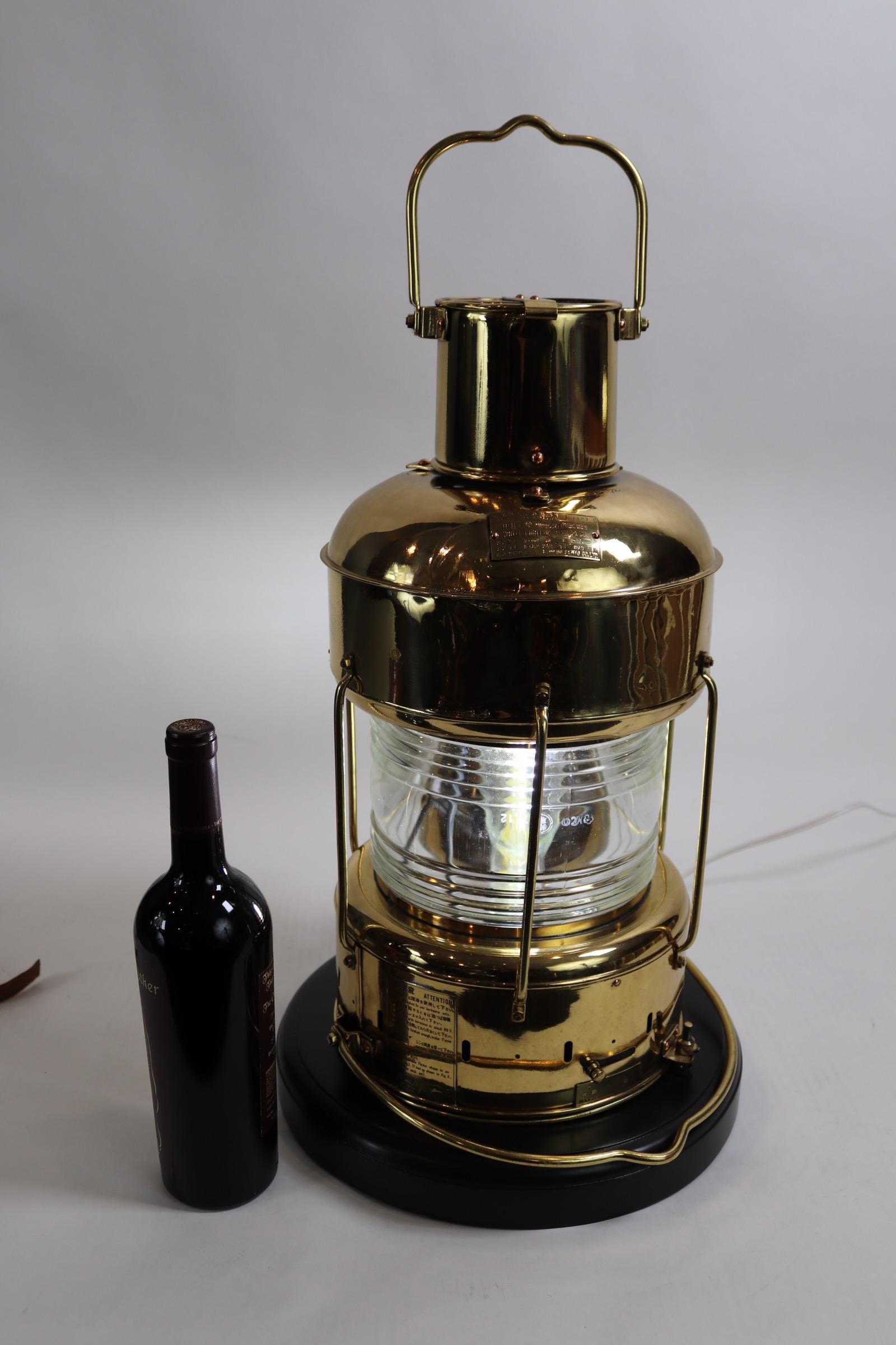 Solid brass highly polished and lacquered ships anchor lantern with Fresnel glass lens. Mounted to a wood base with rich dark finish. With brass makers plate from Japanese manufacturer Nippon Sento. Made in 1977. Lantern has been wired for home