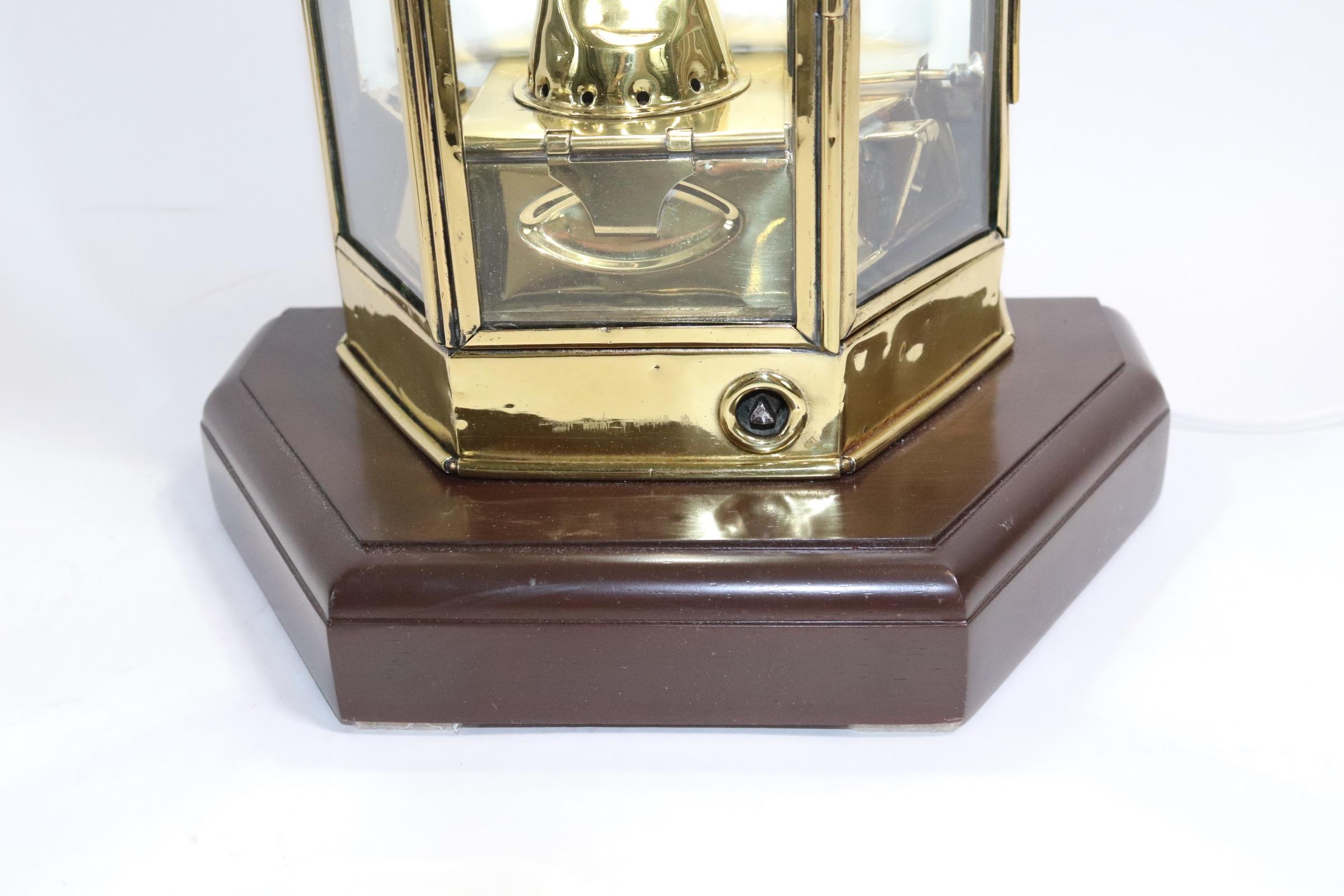Polished and lacquered ships cabin lantern with three glass windows, hinged door, mounted to a thick wood base with rich dark finish. Lantern retains its original burner and is electrified from above for home use. Some dents and dings. Weight is 13