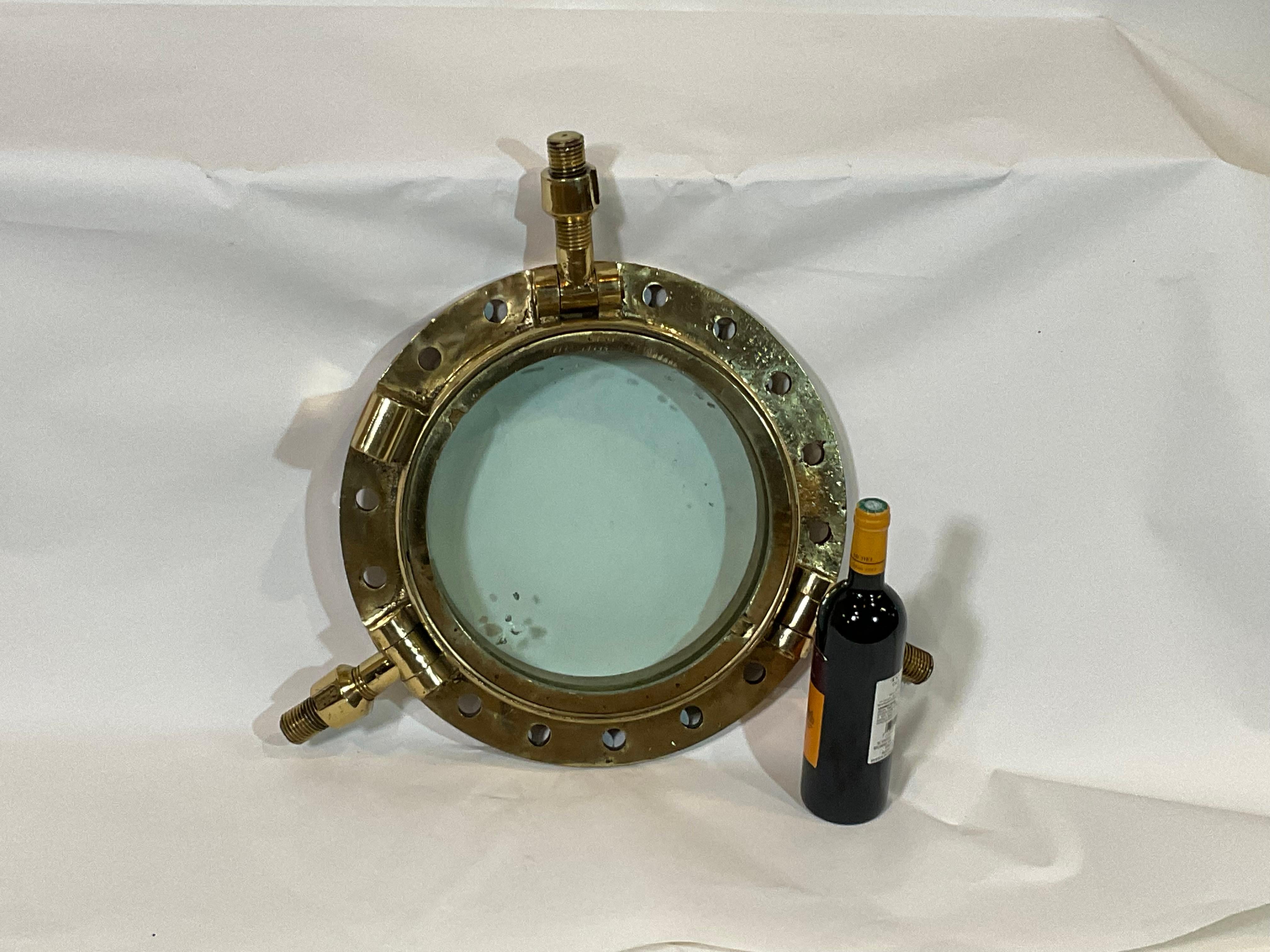 Highly polished ships porthole with lacquered finish. Early 20th century very heavy relic with tempered glass. The original glass shows imperfections from years at sea. Pierced with many mounting holes. Three unusual bras mounting dogs. This is