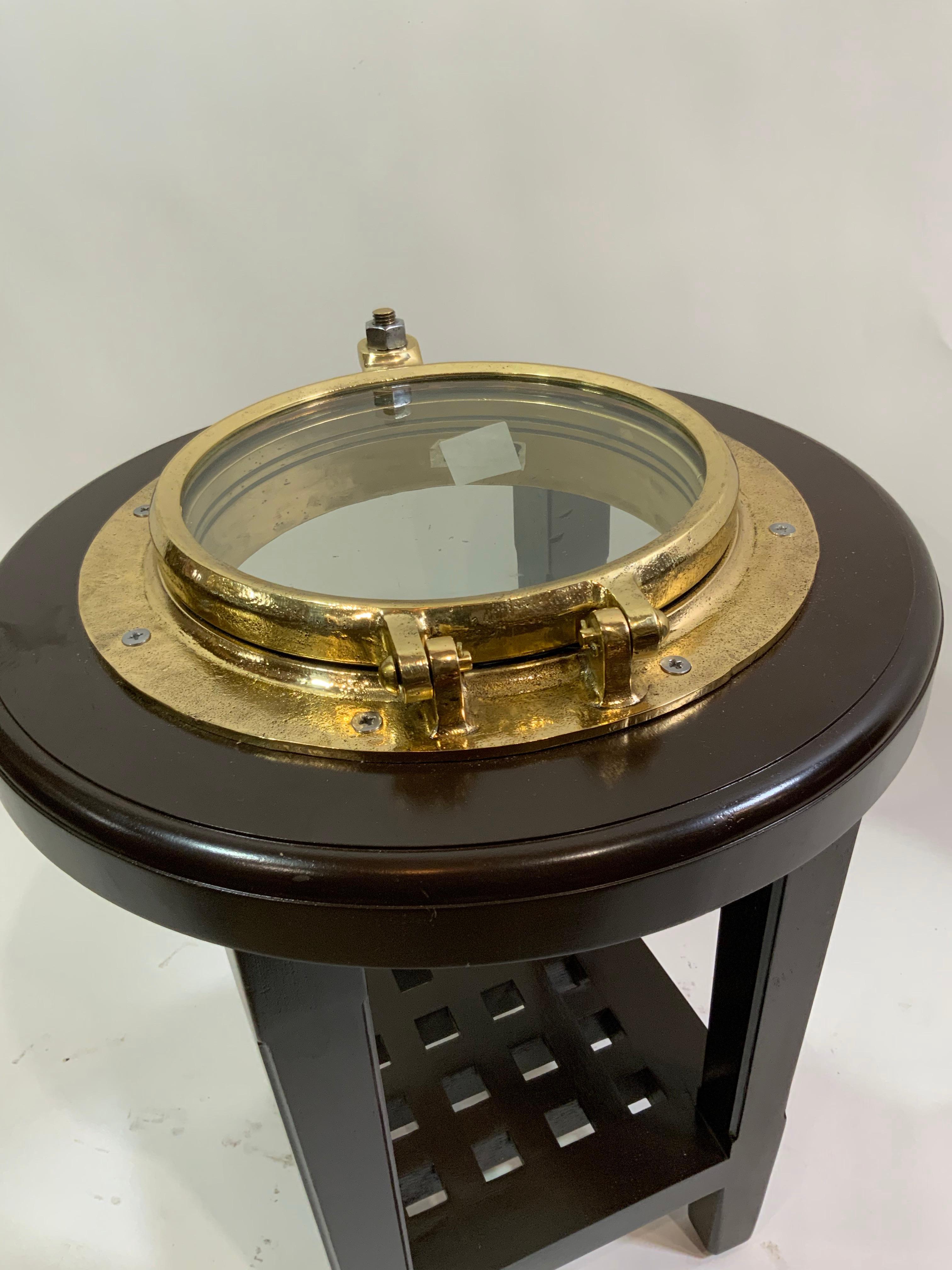Ships porthole that has been meticulously polished and lacquered, then mounted into a mahogany table stand. Weight is 33 pounds.Measures: Diameter of table is 24 inches. Height is 19 tall.