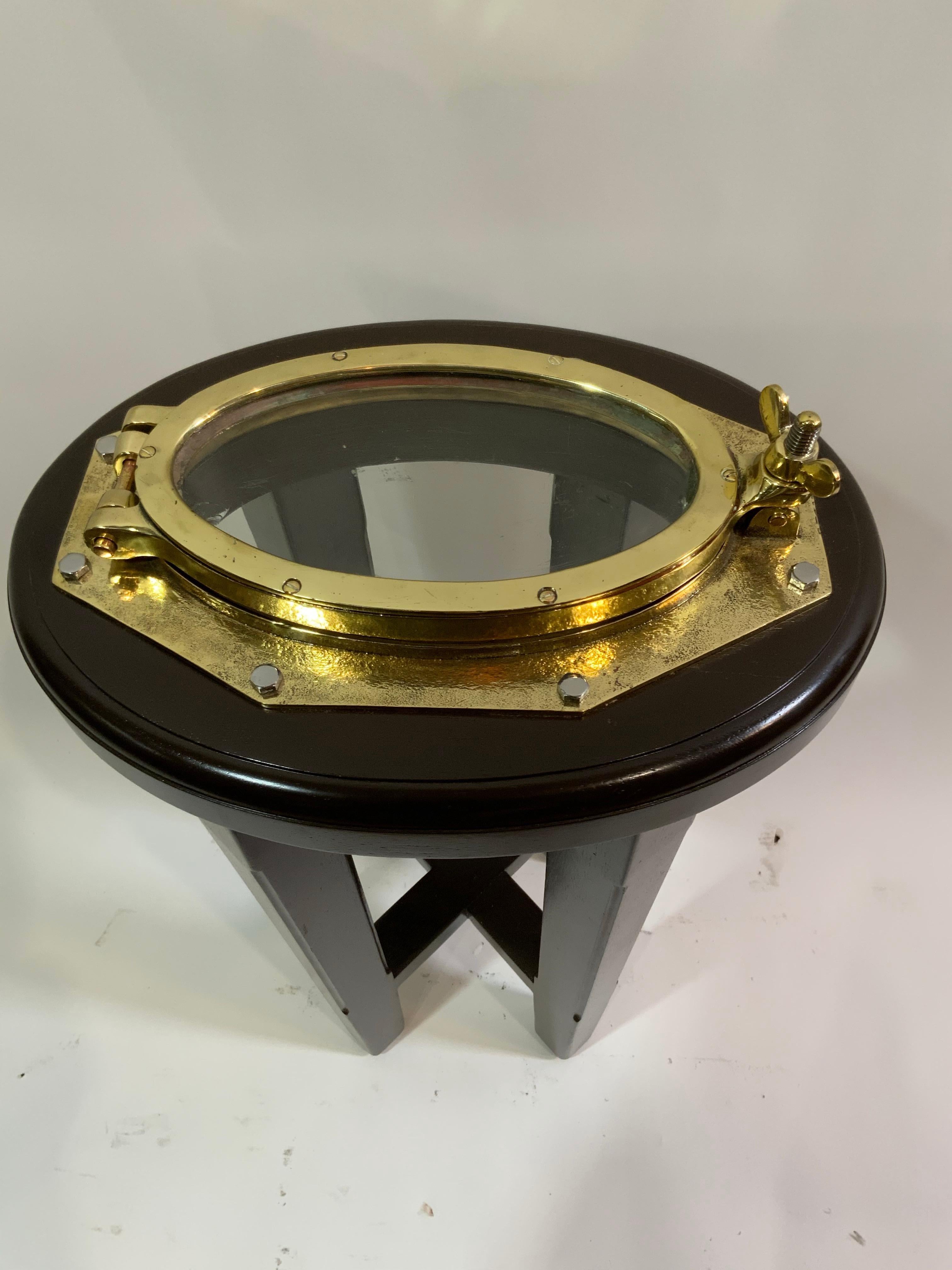 Solid brass boat porthole that has been meticulously polished and lacquered, then mounted to a custom mahogany table stand. Oval glass. Weight is 17 pounds. Height is 24 inches and width 15 by 11.