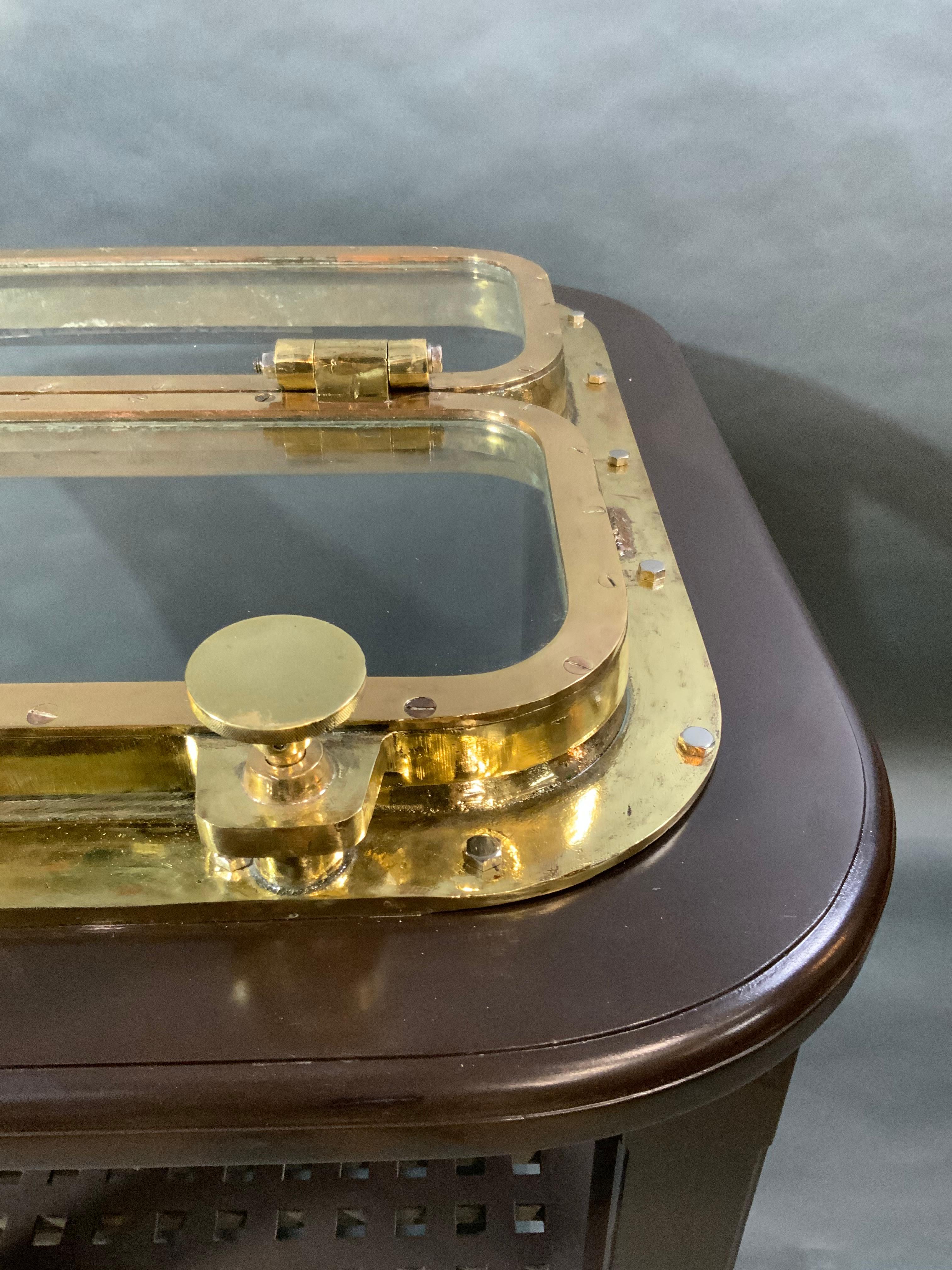 Table de hublot de navire en laiton massif. Il s'agit d'un grand et substantiel hublot de bateau monté sur une table à hauteur de bar avec quatre pieds et une étagère en caillebotis de bateau. Hautement polie et laquée. Le poids est de 130 livres.