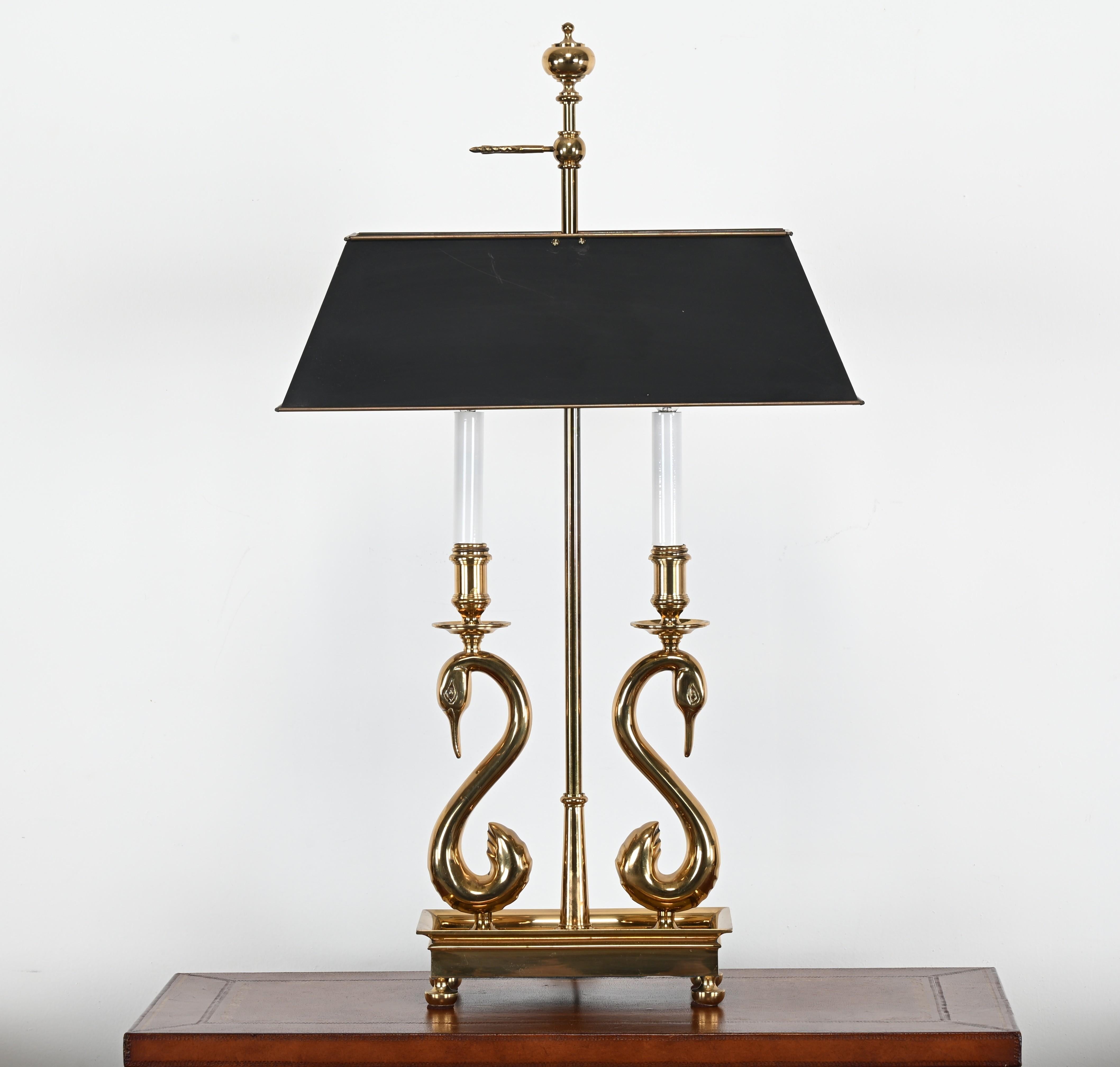 This elegant vintage bouillotte lamp features a striking solid brass construction, showcasing two gracefully curved swan motifs that form the candle arms, a hallmark of the classic French Empire style. The lamp is mounted on a sturdy brass base with