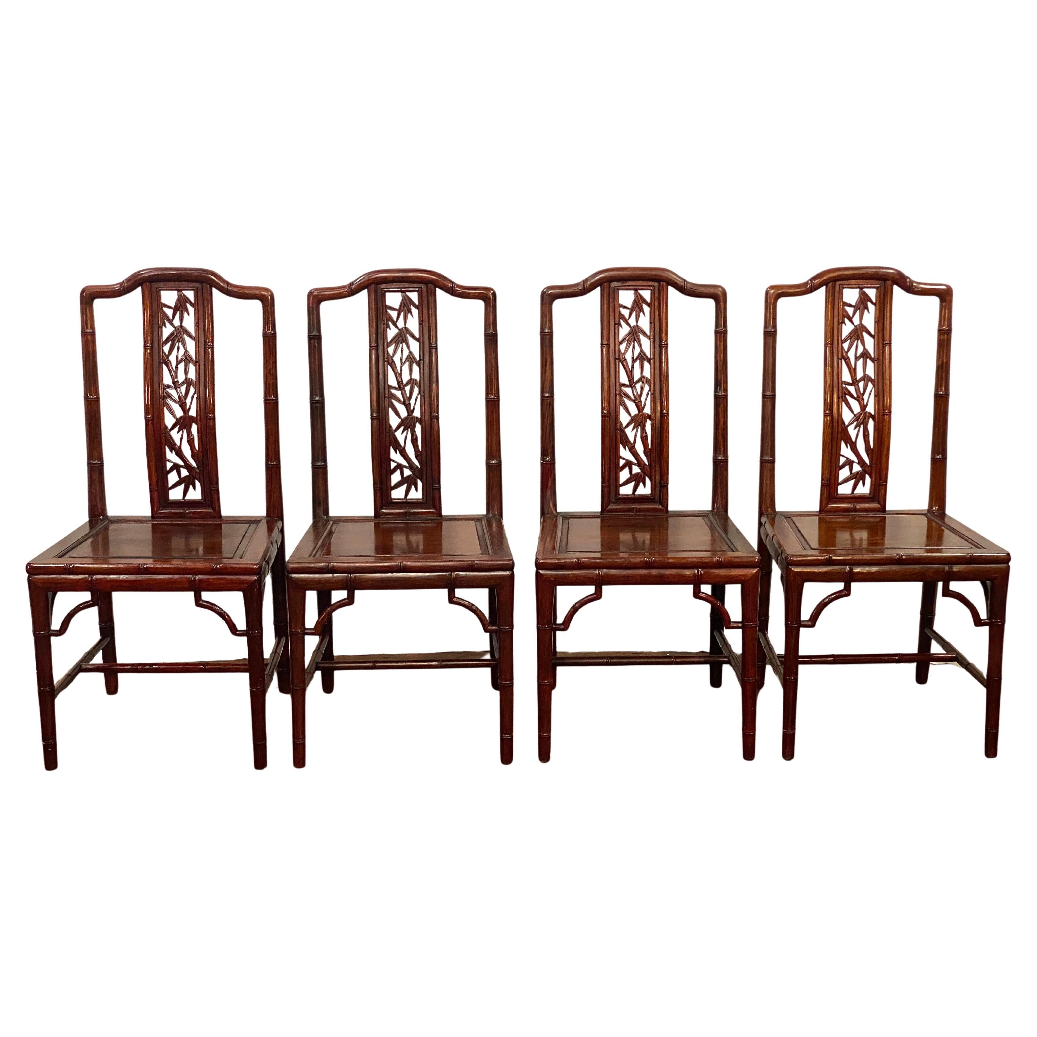Four finely carved and exceptional solid rosewood faux bamboo dining chairs. These chairs feature solid wood construction, carved faux bamboo leaf back splats and faux bamboo stalk legs, sides and upright back supports. Circa 1980. A comfortable