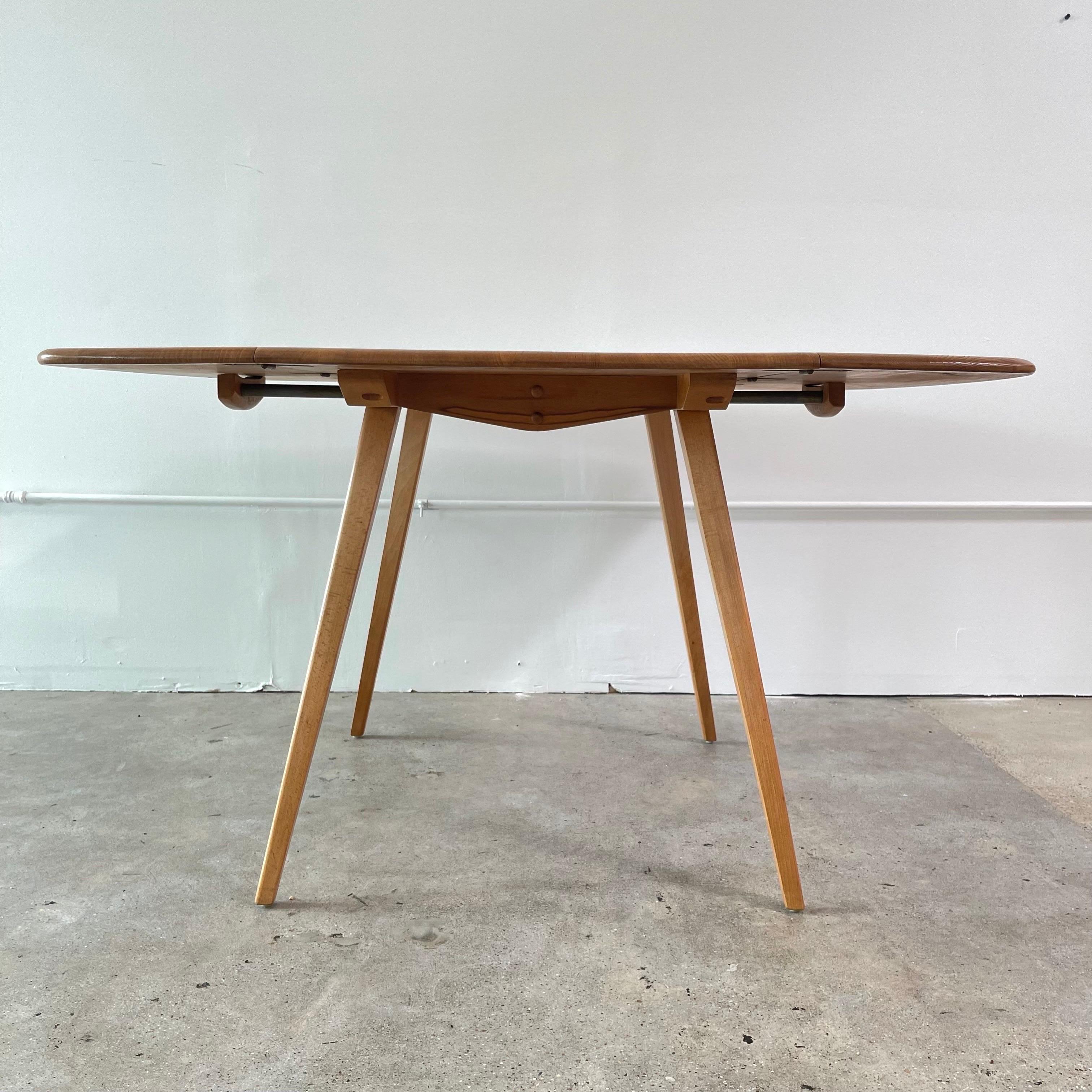 Solid elm drop leaf table with splayed legs made of beech wood. Made by Ercol in the 1960’s by Lucian Ercolani. Sharp angular legs contrast nicely with the soft corners of the table top.